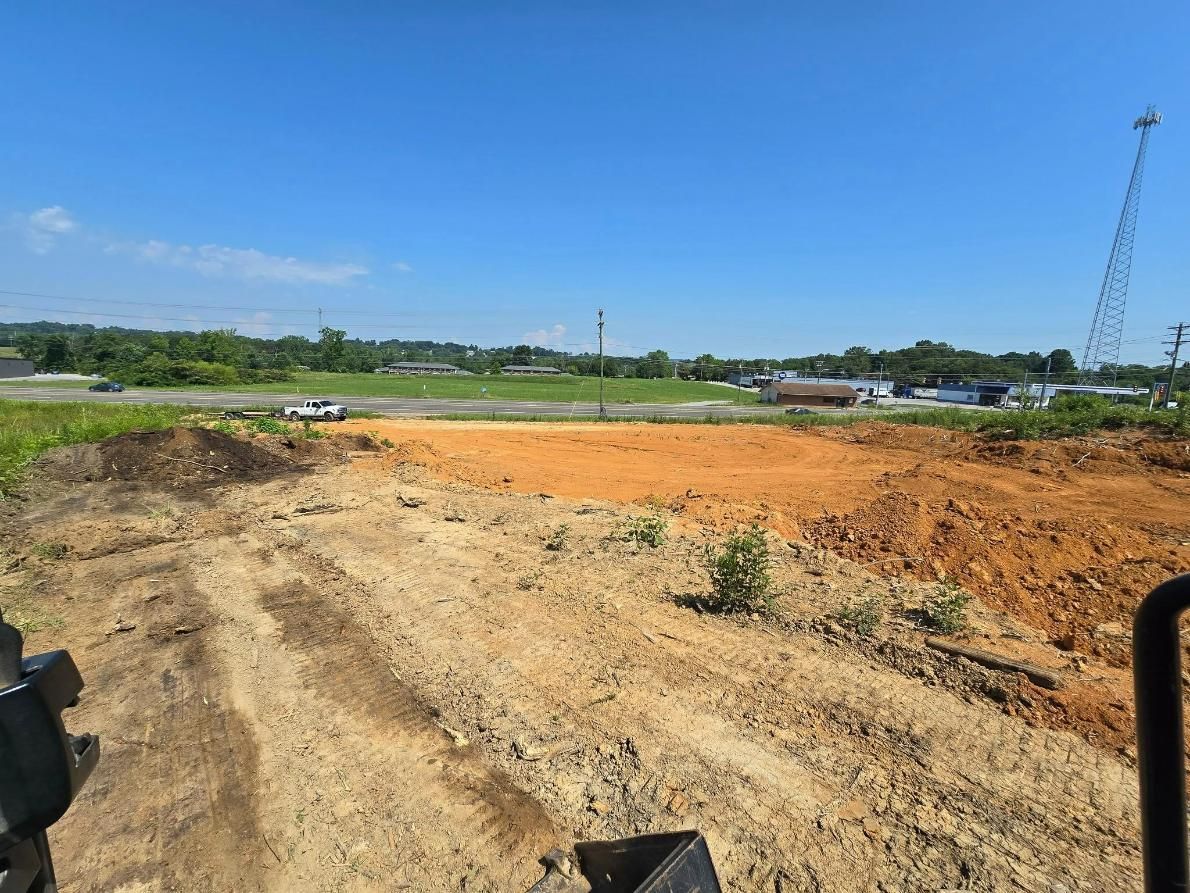 Dirt lot cleared for construction under a blue sky; a telephone pole and trees are visible in the background.