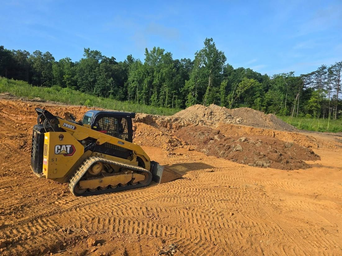 Yellow Caterpillar skid steer on a dirt site, trees in the background, under a blue sky.