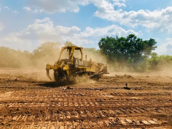 Yellow bulldozer clearing a field, kicking up dust, under a blue sky.