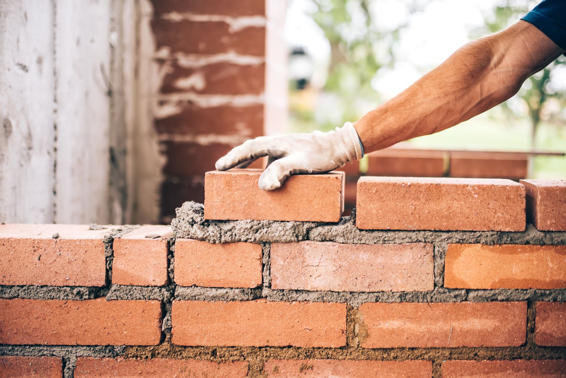 Gloved hand placing a brick on a partially built brick wall outdoors
