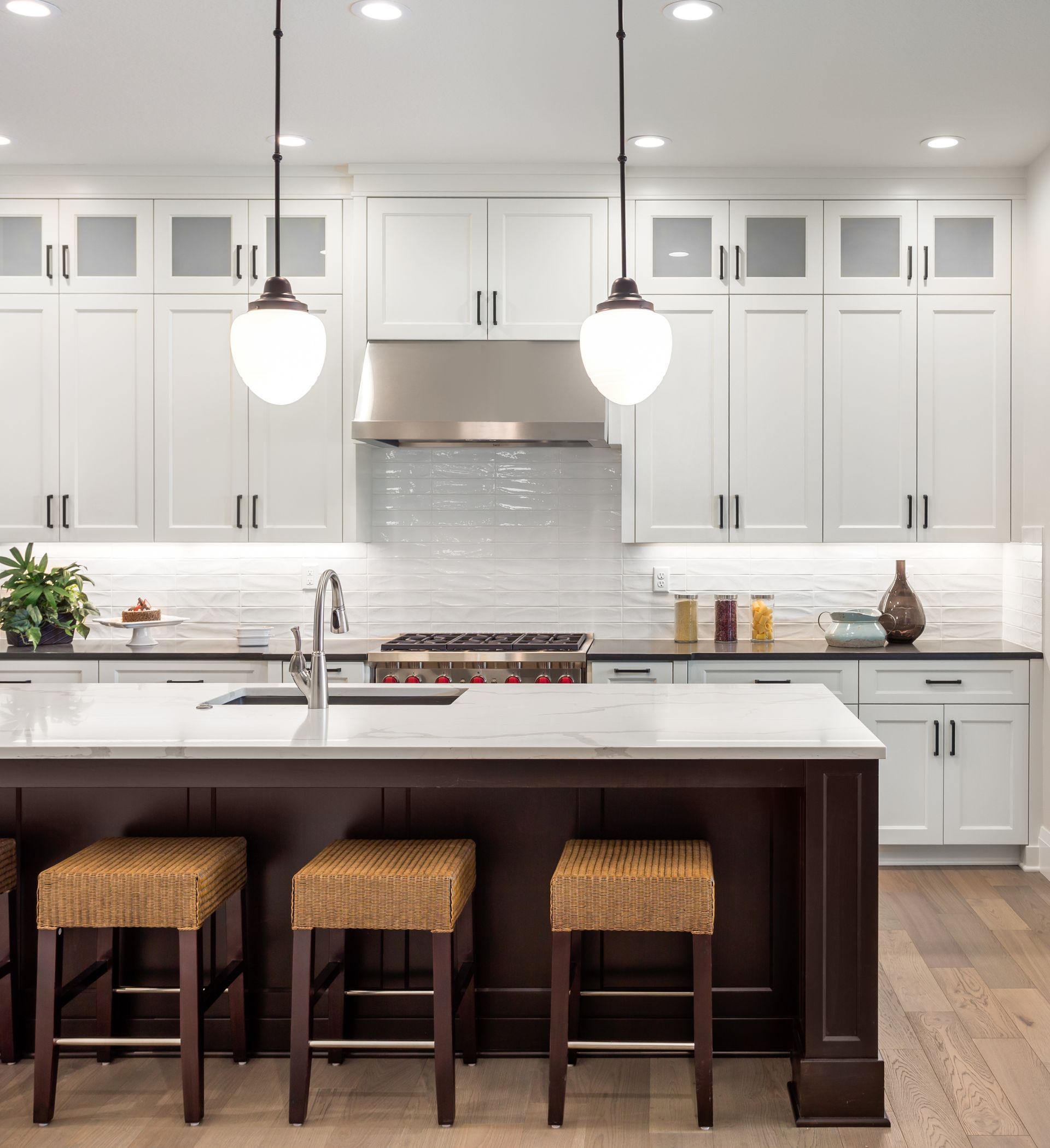 Bright white modern kitchen with island, three woven stools, pendant lights, and stainless steel range hood