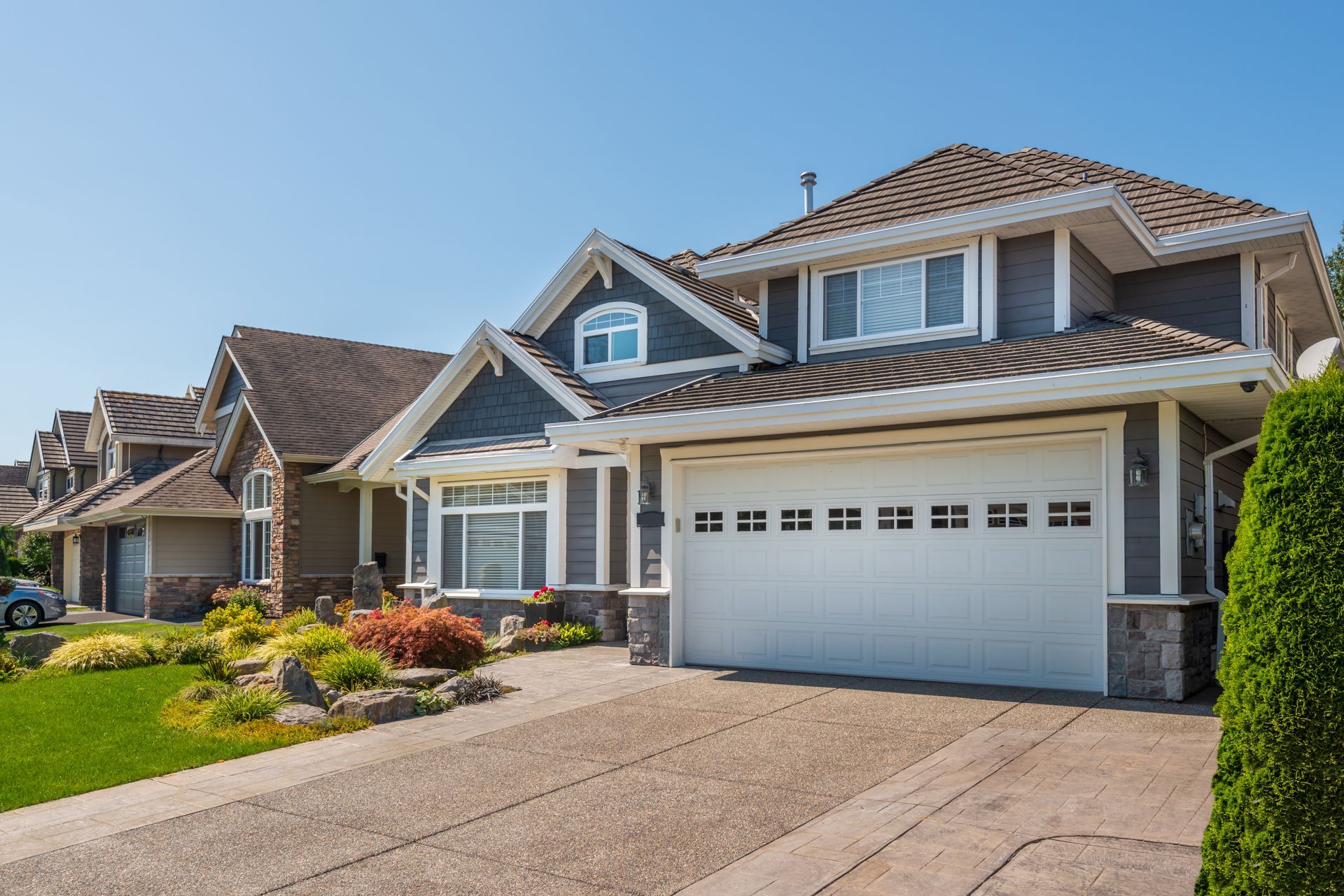 Suburban houses with attached garages and landscaped lawns on a sunny street Suburban houses with attached garages and landscaped lawns on a sunny street