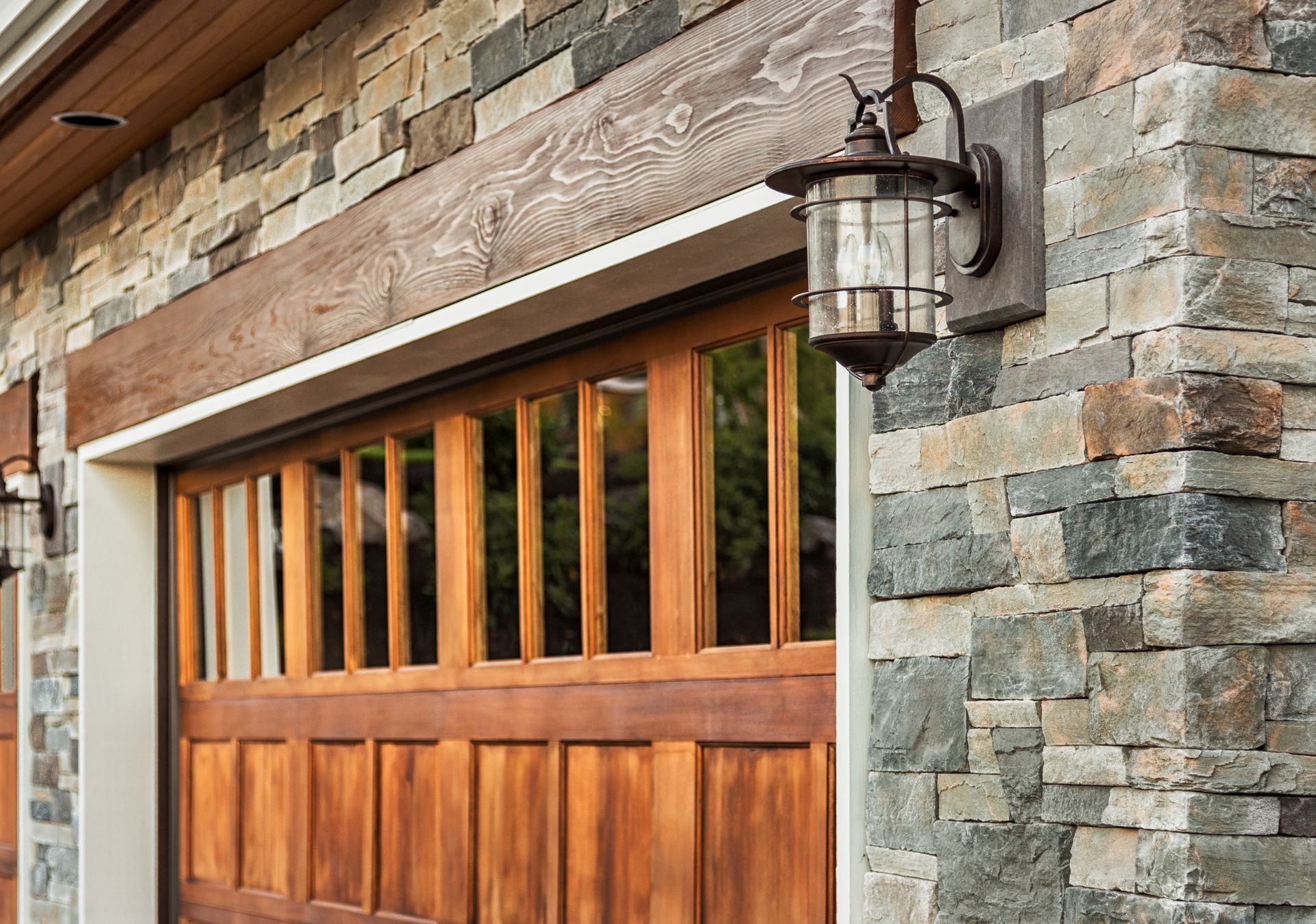 Wooden garage door framed by stone and wood siding with a rustic wall lantern.