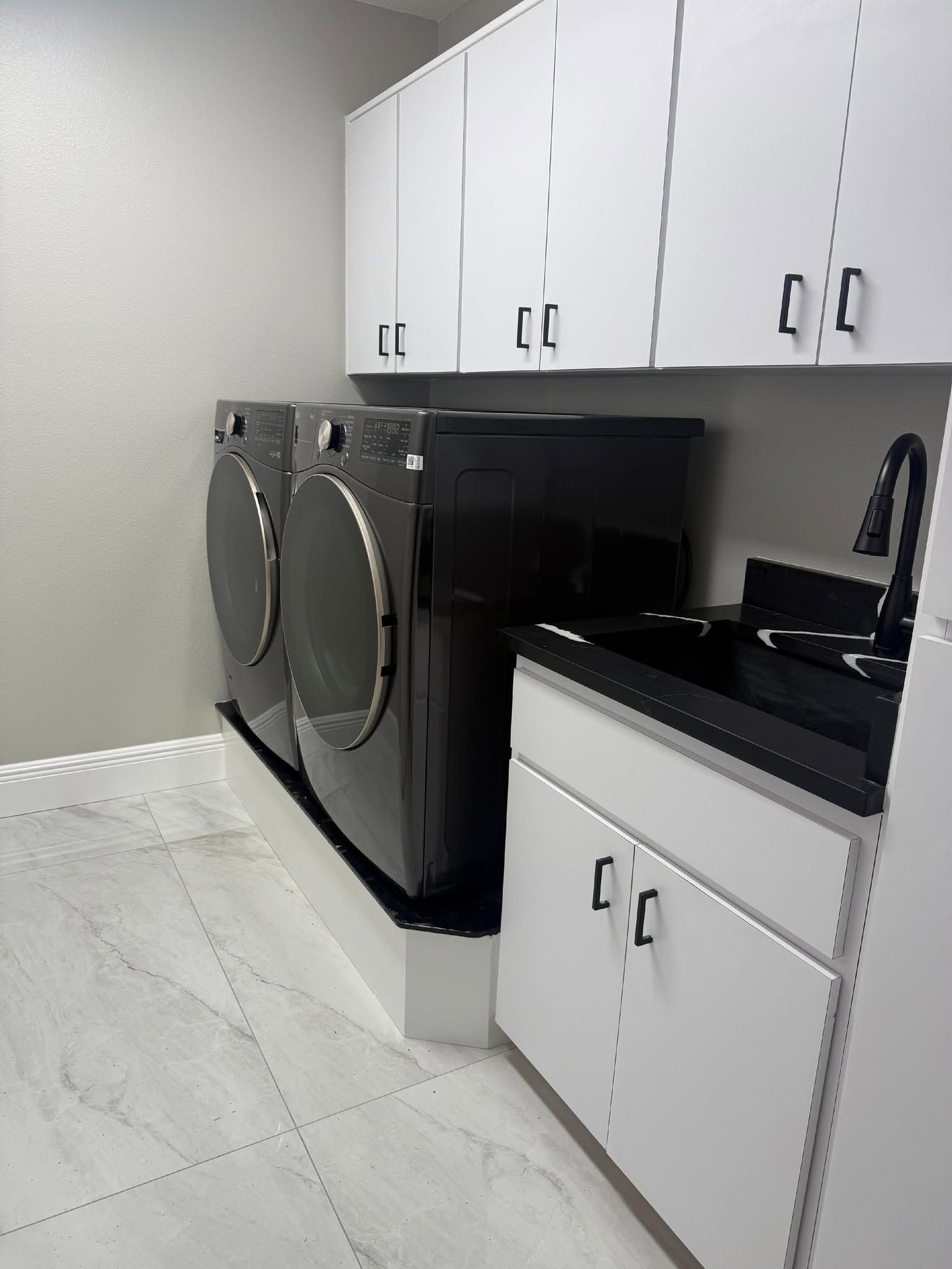 Laundry room with white cabinets, black countertop, and silver washer and dryer on a light tile floor