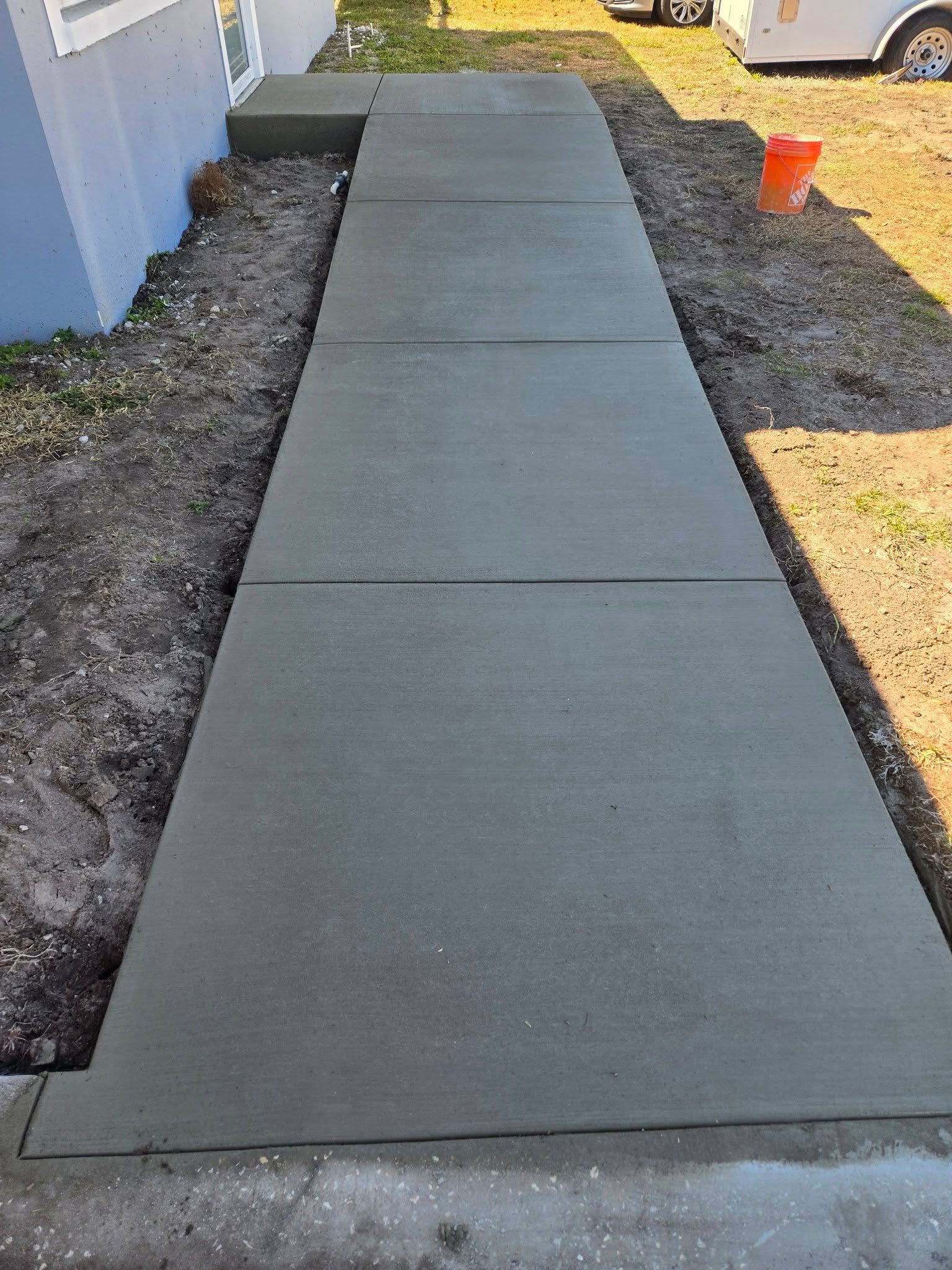 Concrete sidewalk beside a building, with gravel edges and a small orange cone in the distance.