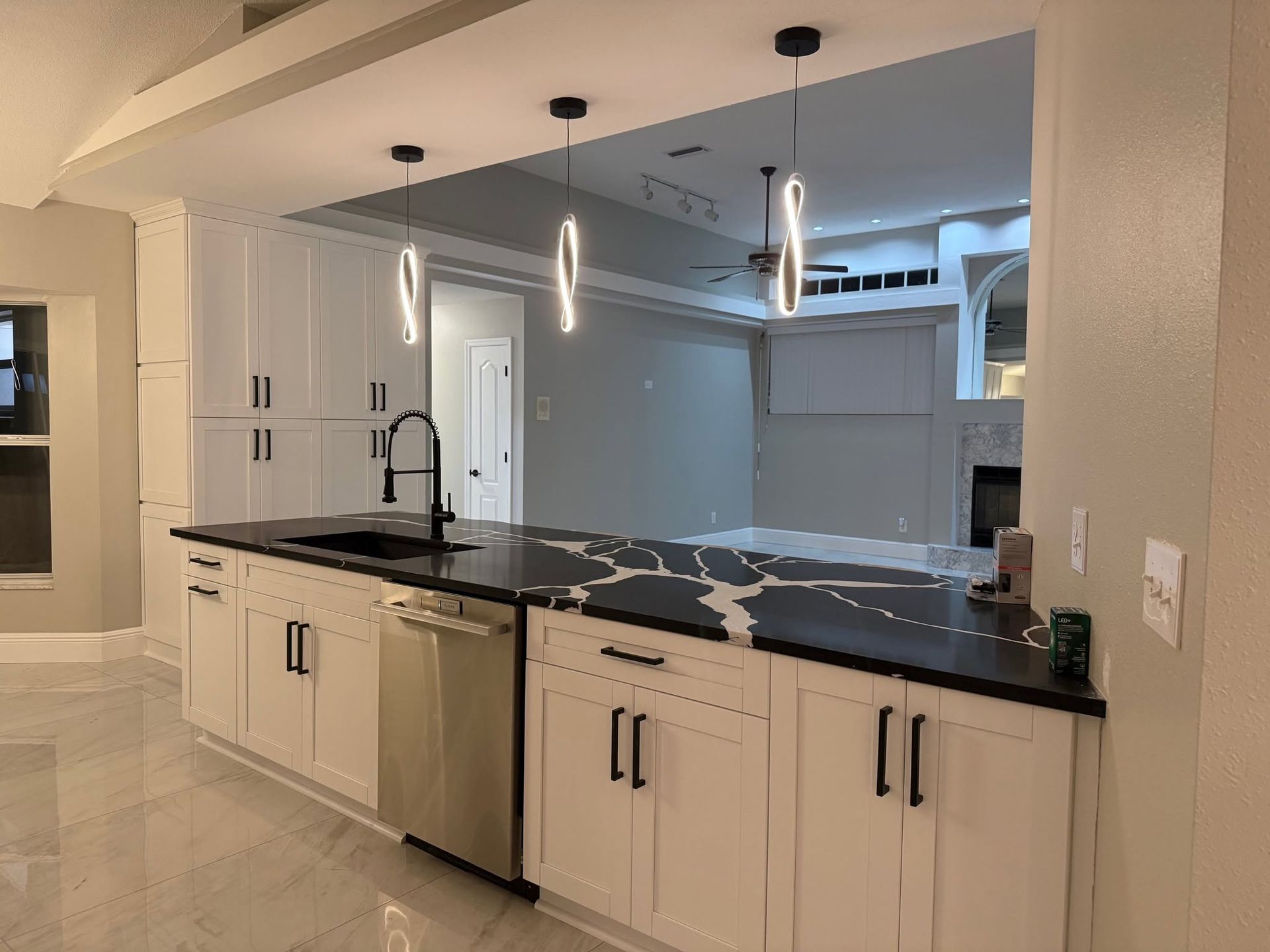 Modern white kitchen with black countertops, island sink, and pendant lights