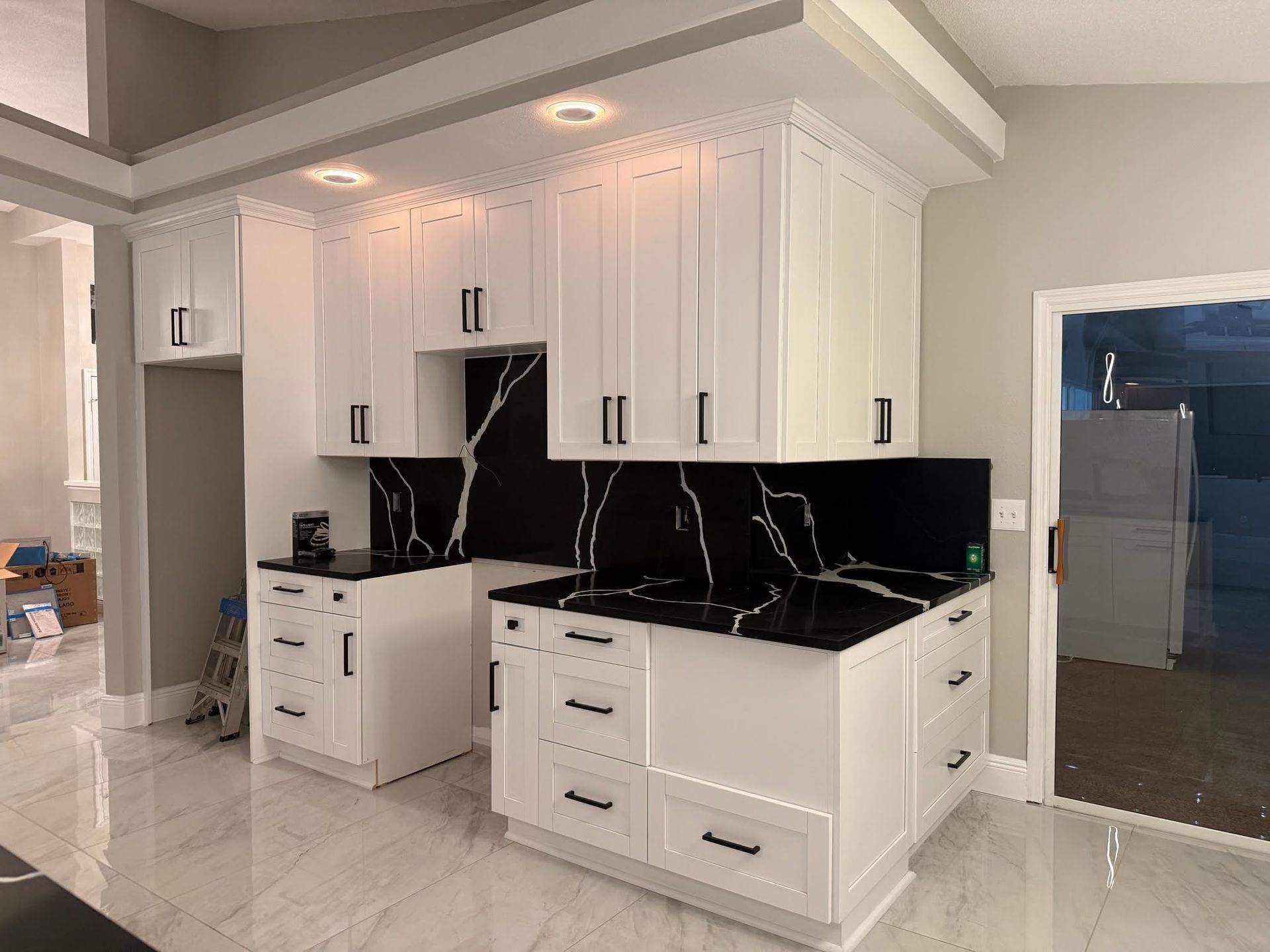 Modern white kitchen with black countertops, black backsplash, and glossy tile floor Modern white kitchen with black countertops, black backsplash, and glossy tile floor
