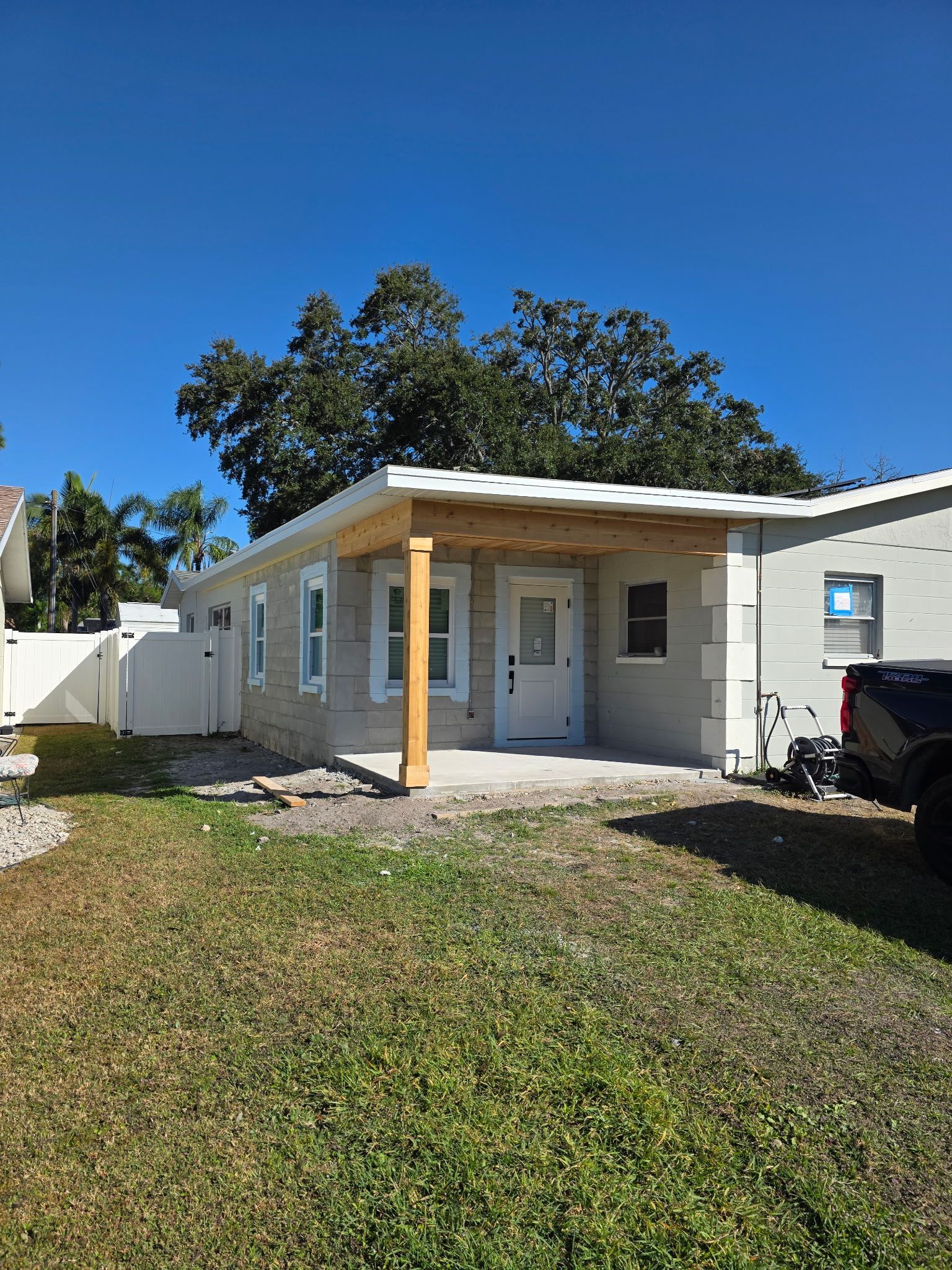 Small white house with a covered porch, grassy front yard, and parked vehicle under a blue sky Small white house with a covered porch, grassy front yard, and parked vehicle under a blue sky