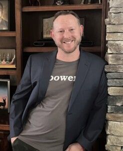 A man in a suit and a t-shirt is standing next to a stone wall.