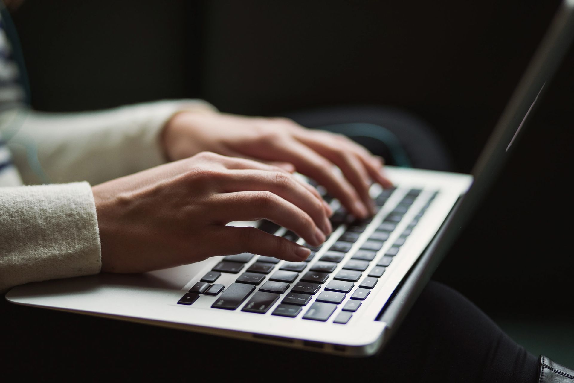 Close-up of hands typing on a silver laptop keyboard.