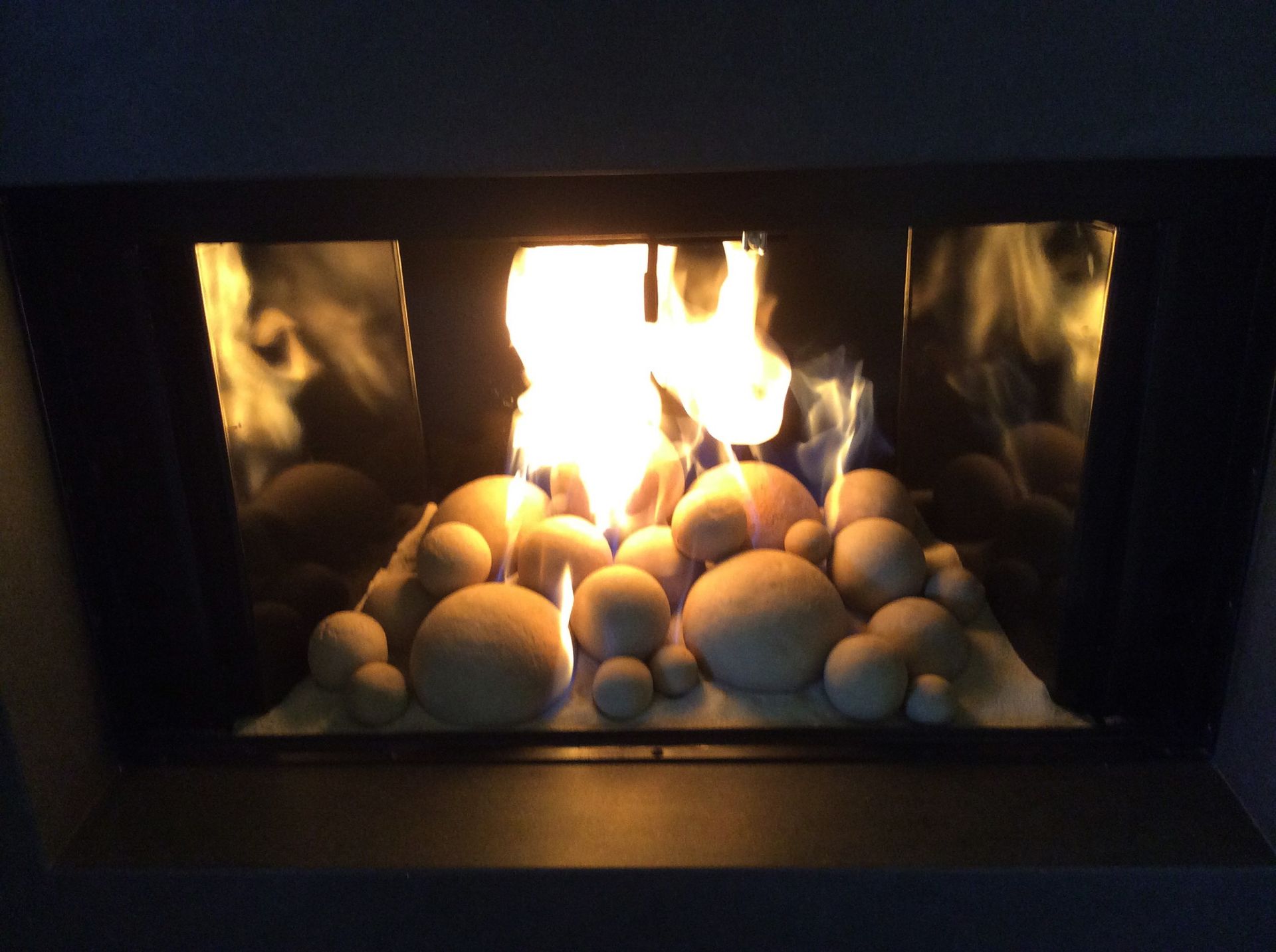 Fireplace with flames rising above ceramic spheres, enclosed in a dark frame.