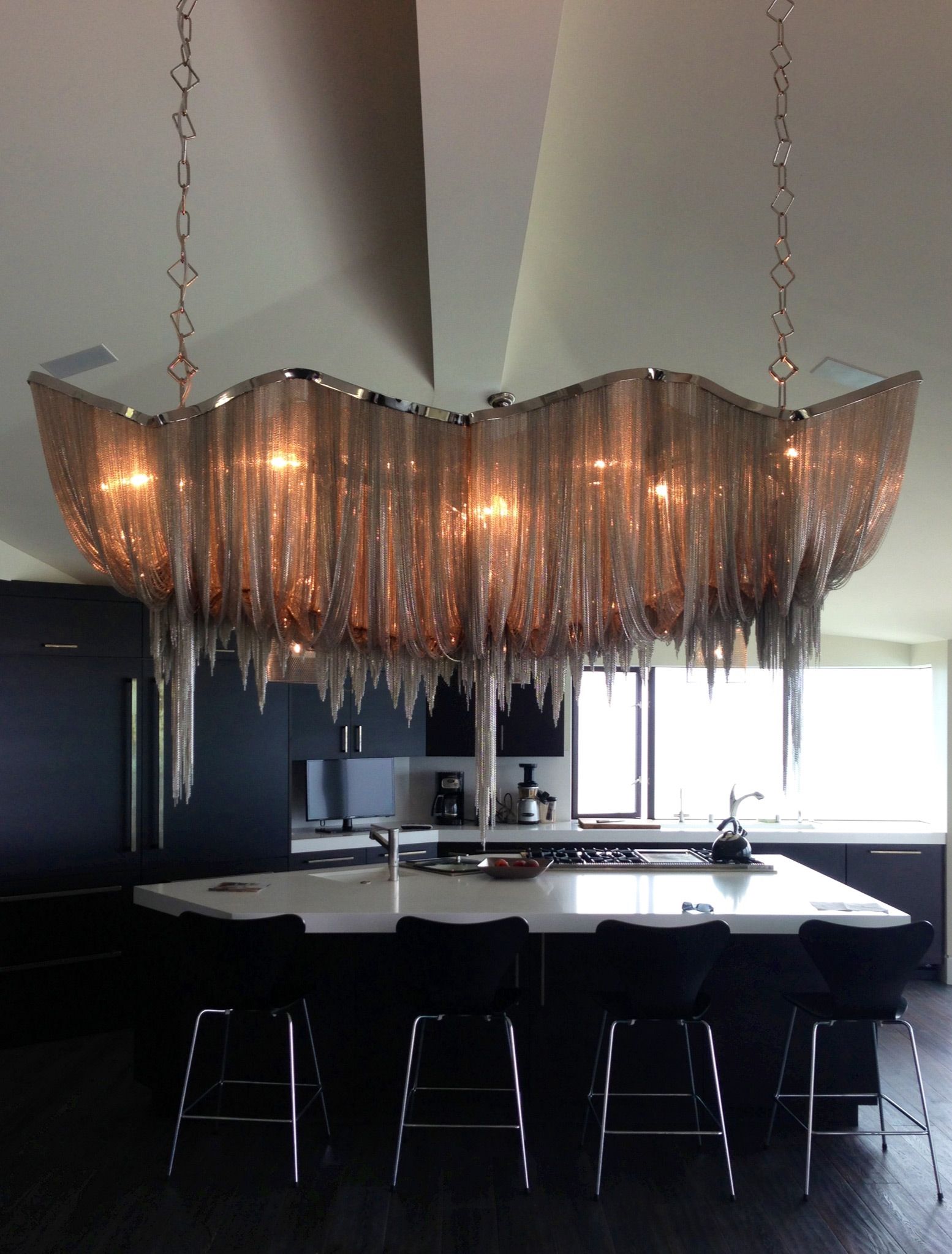 Kitchen with large, ornate silver chain chandelier above an island with bar stools.