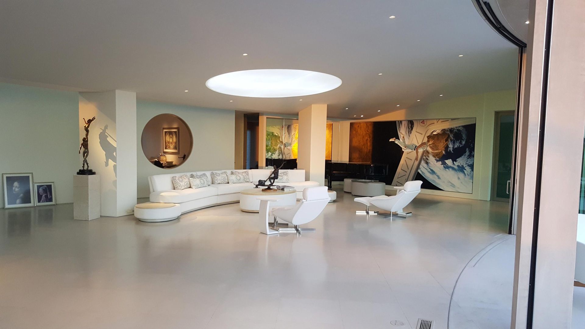 Spacious, modern living room with white curved sofa, art, and large round skylight.