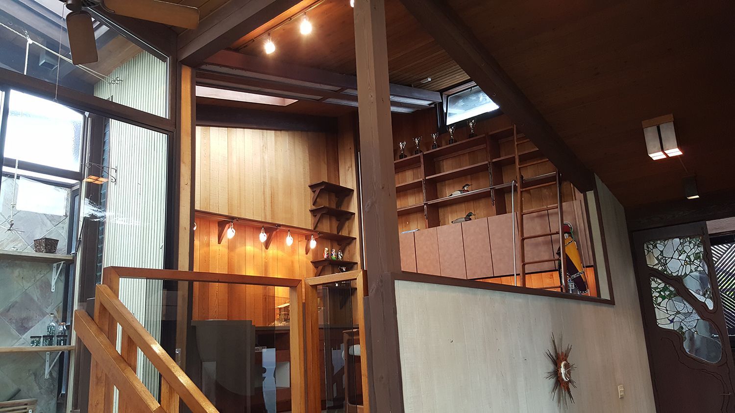 Interior view: Wooden stairs leading to a loft with shelves. Warm lighting on wood paneling.