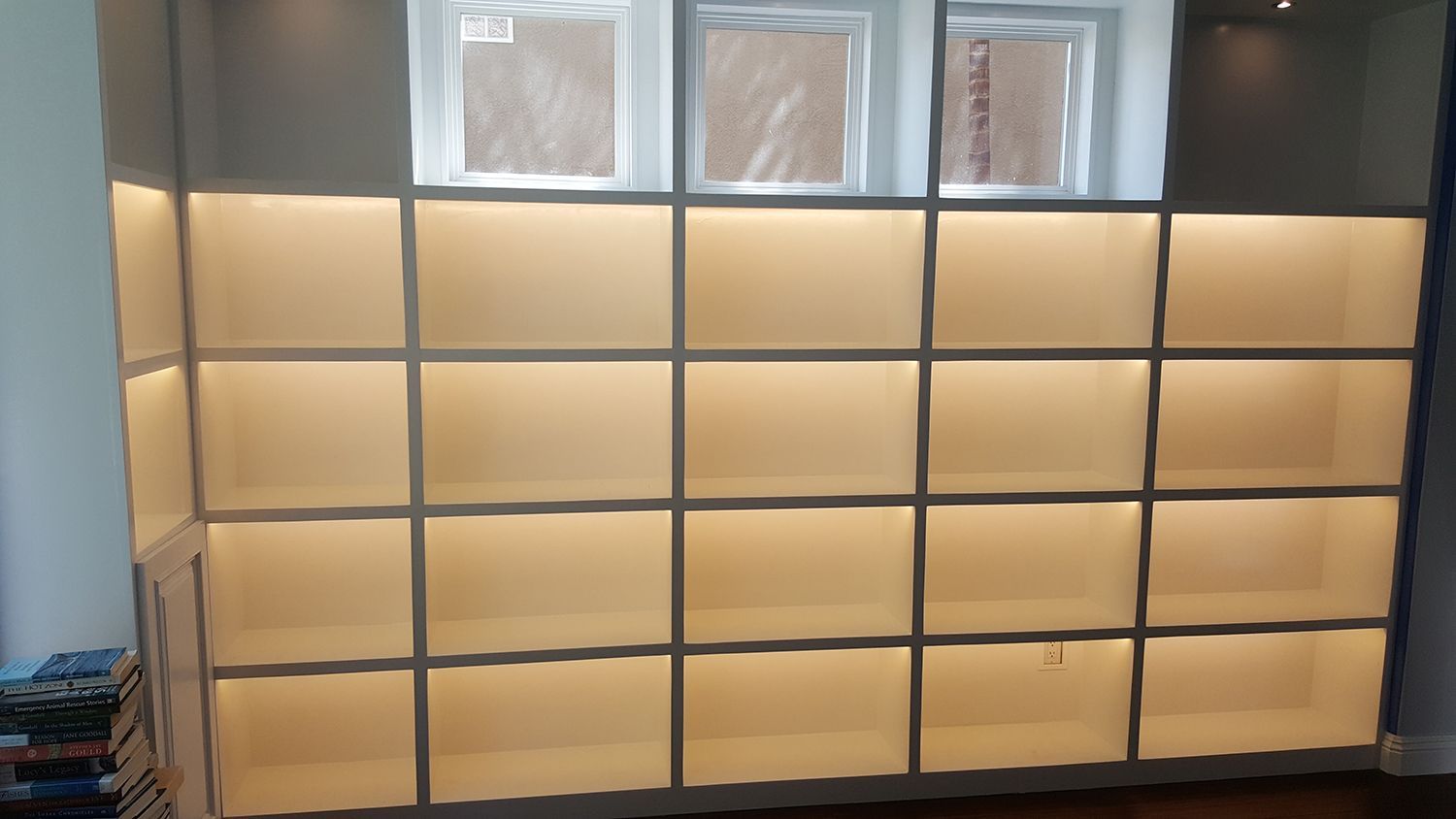 Built-in bookshelf with illuminated squares below two windows; shelves are empty.