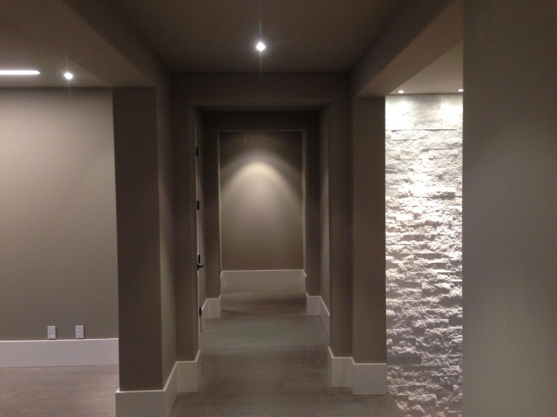 Long hallway with recessed lighting, gray walls, and a stone accent wall.