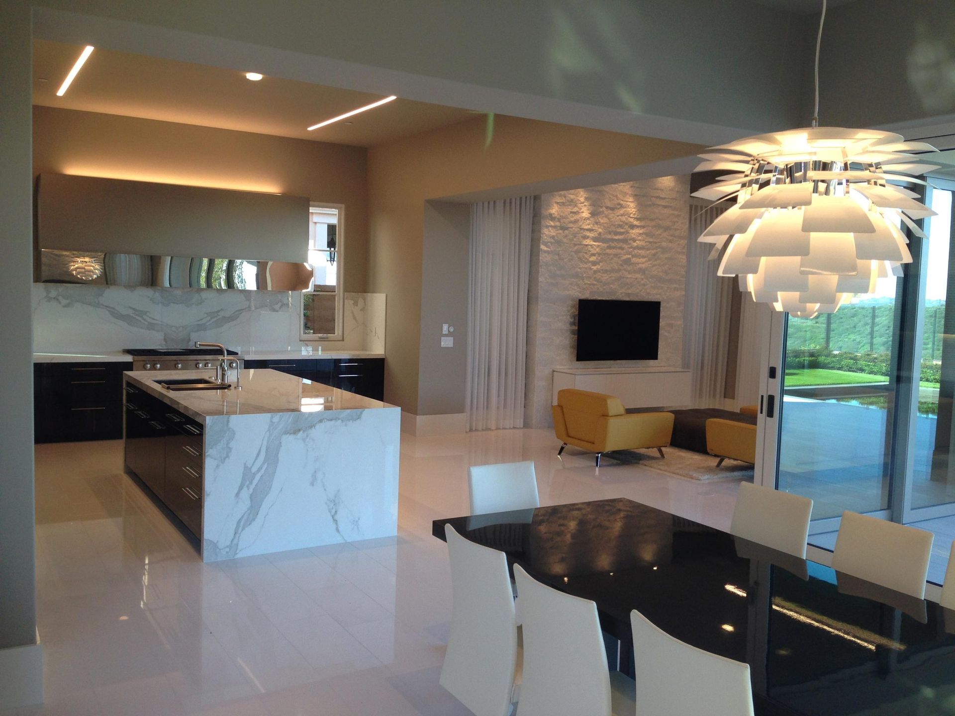 Modern open-plan kitchen and living area with marble island, black cabinets, and a dining table.