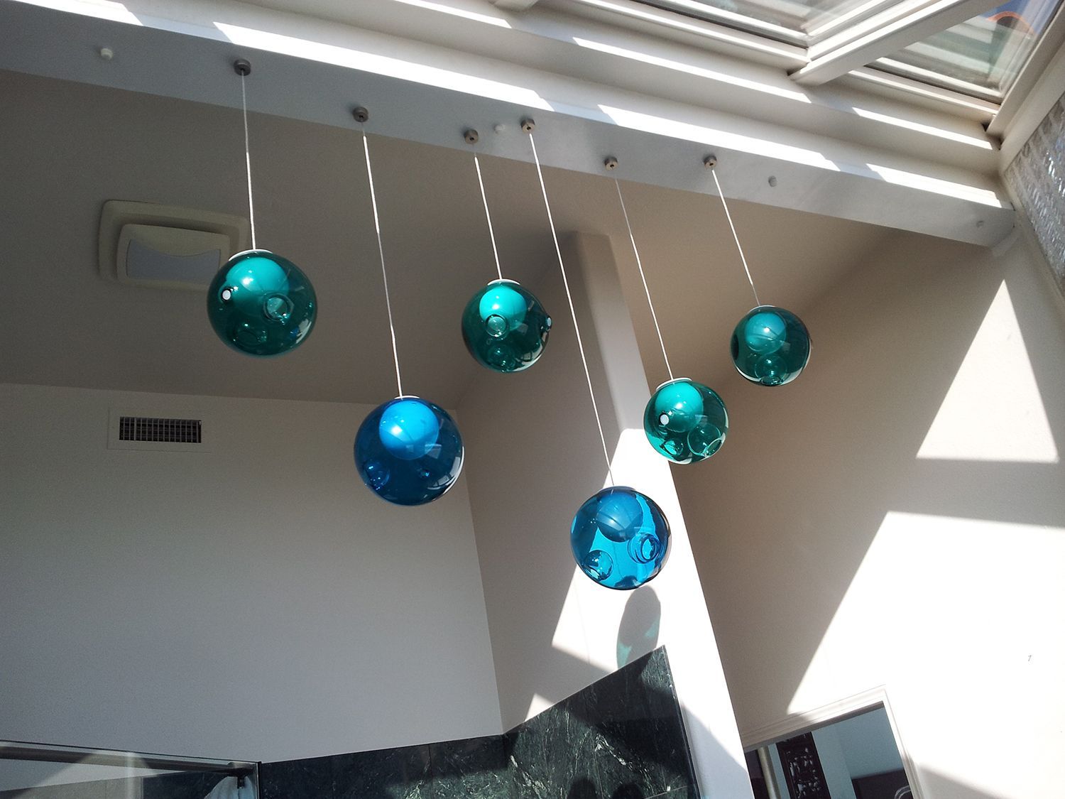 Hanging teal and blue glass spheres suspended from a ceiling in a light-filled room.