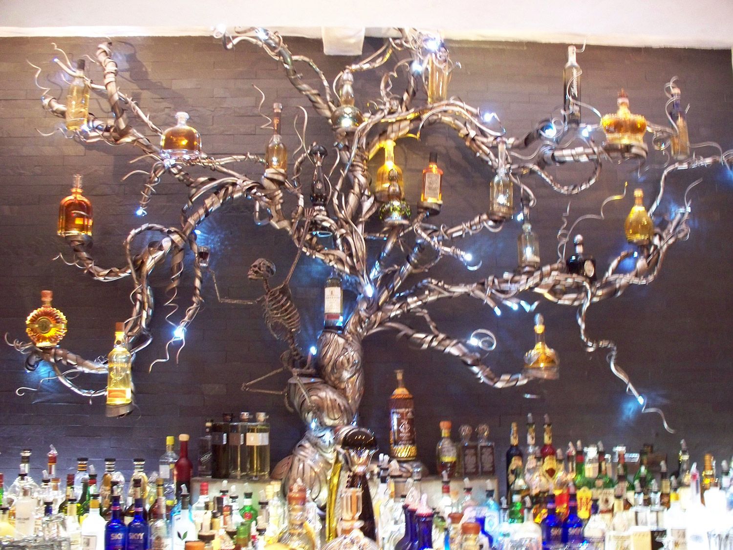 A metal tree sculpture holding liquor bottles above a bar.
