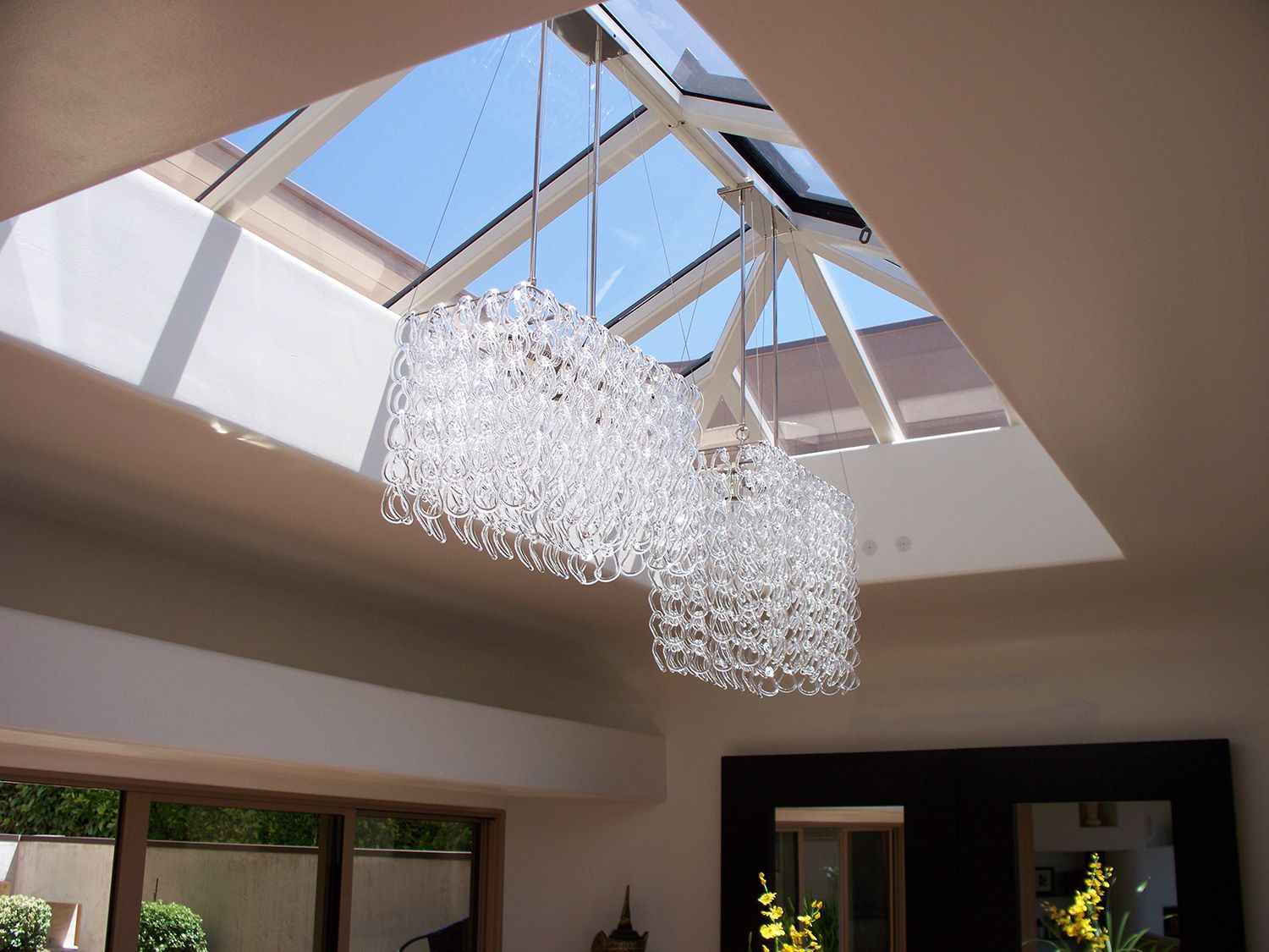Two crystal chandeliers hang below a skylight in a modern room.