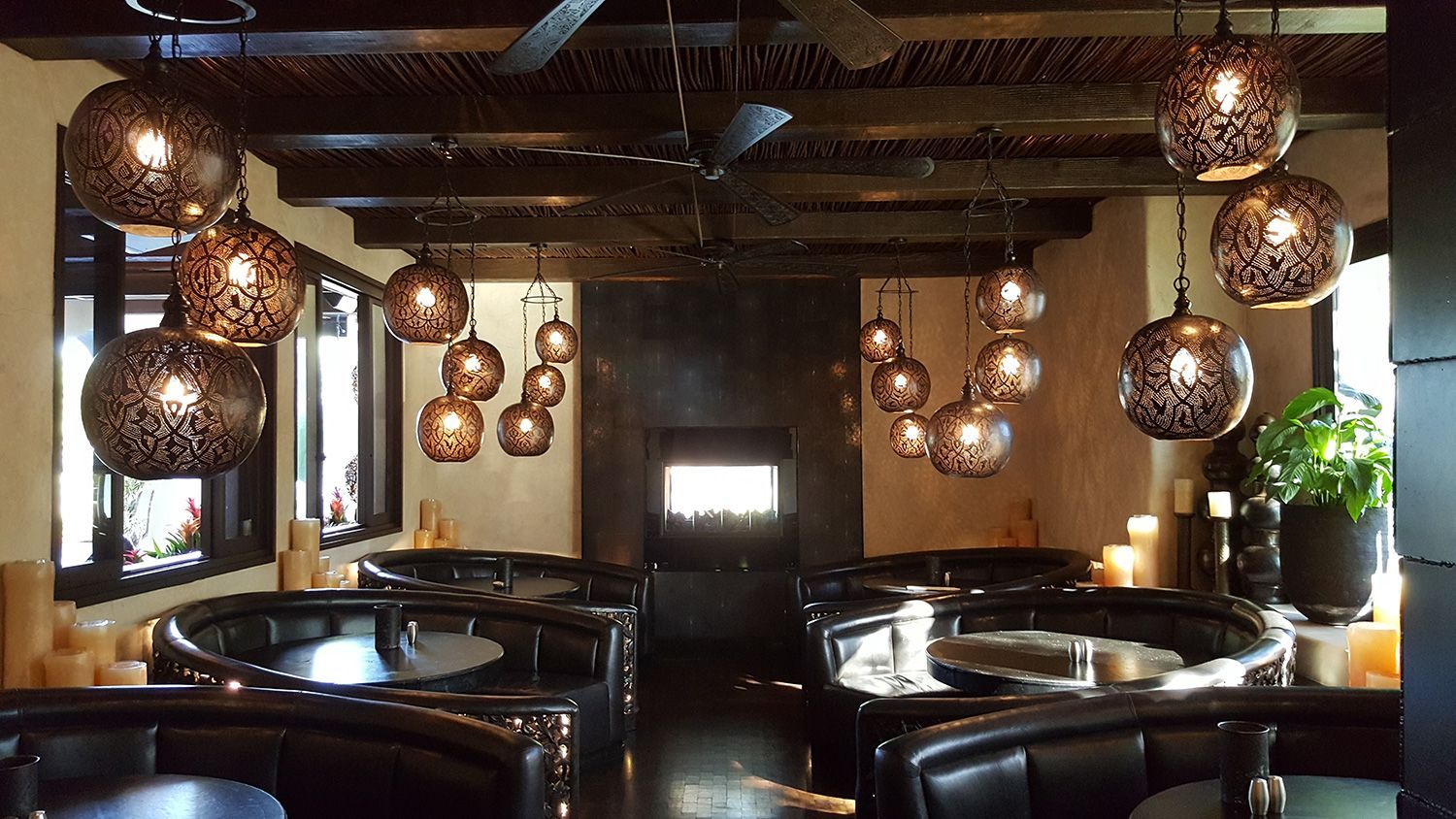 Dark restaurant interior with round booths, decorative hanging lamps, fireplace, and candles.