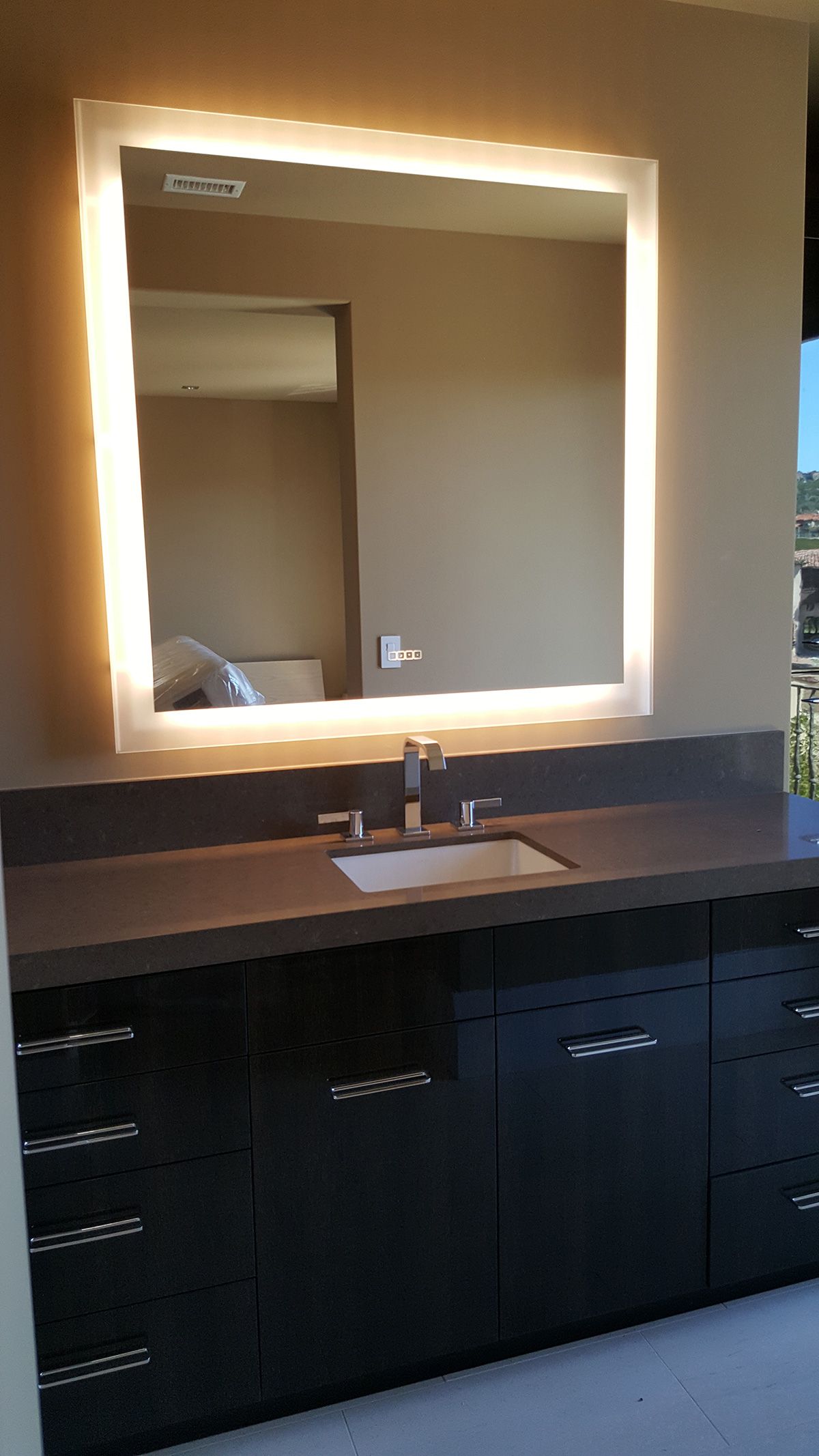 Lit mirror above a dark vanity with a sink and cabinets. Brown walls.
