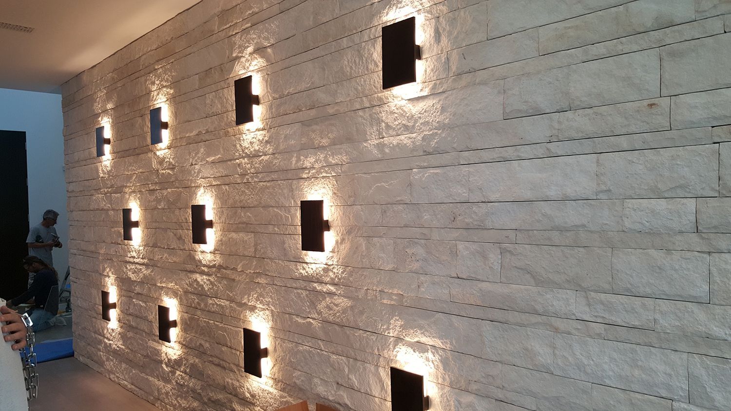 Textured stone wall with inset black square lights casting warm light, indoors.