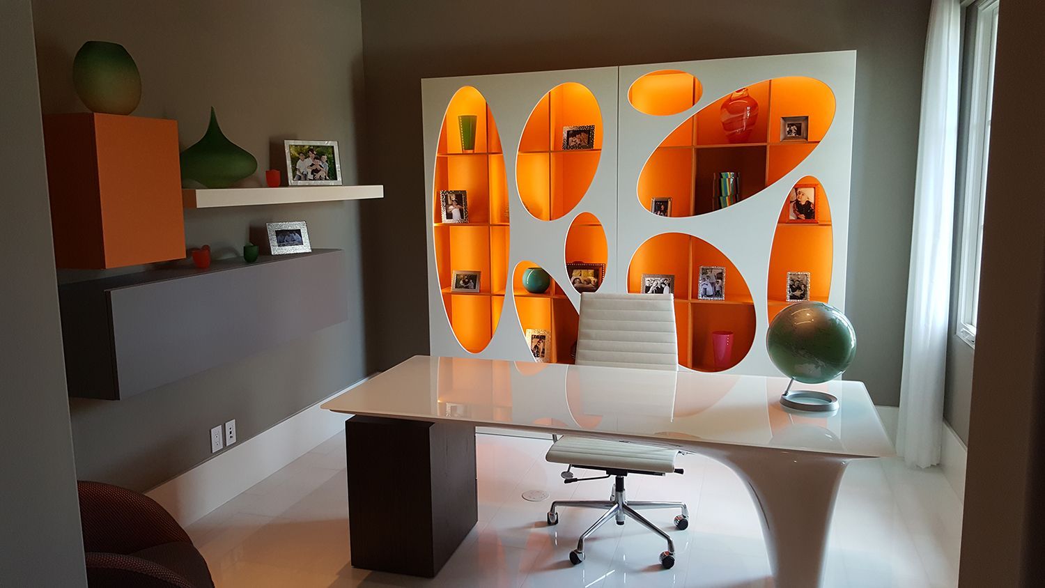 Modern home office with a white desk, orange shelving, and a globe.