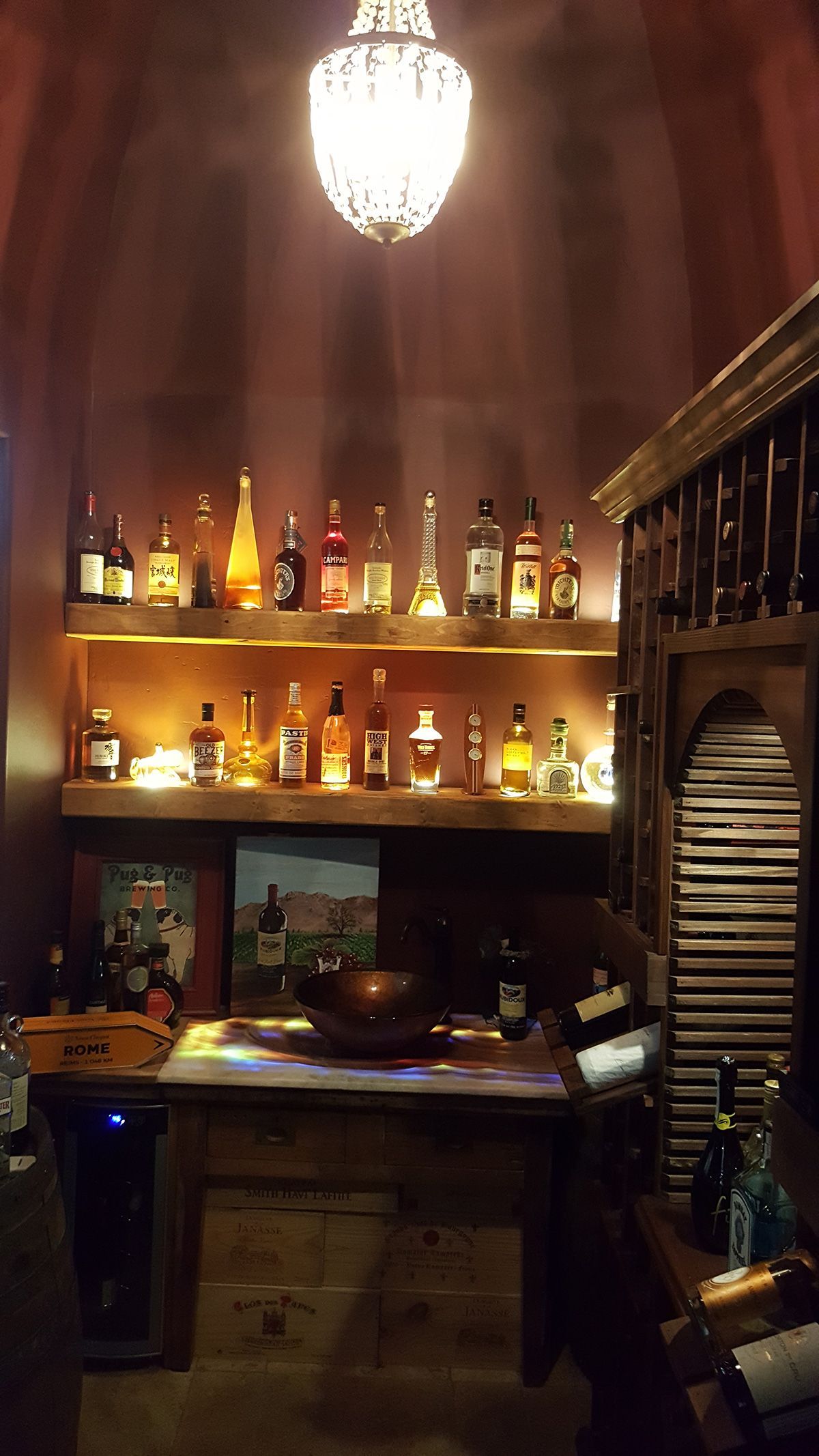 Bar with glowing shelves, bottles, a decorative chandelier, and a wooden table.