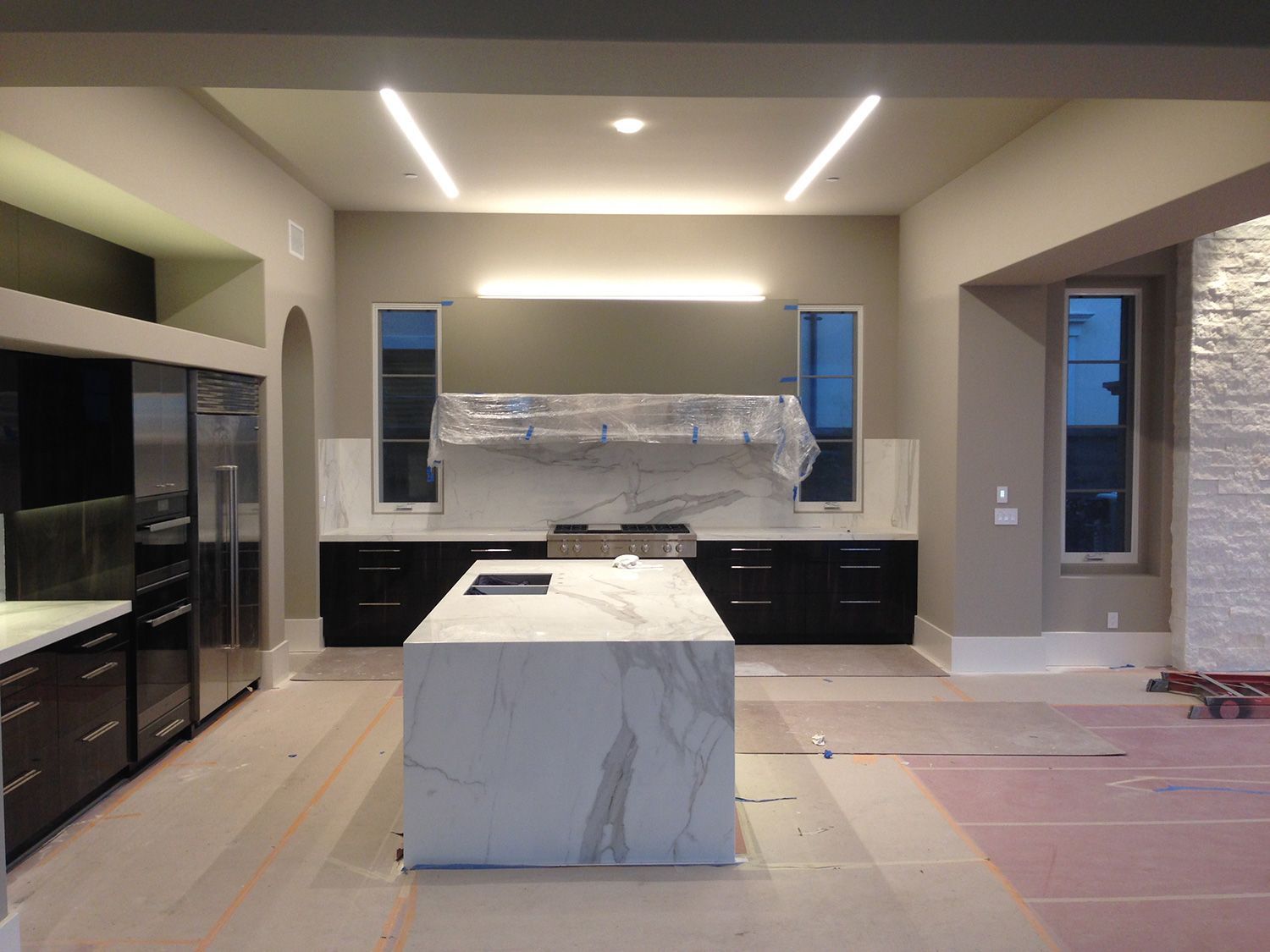 Modern kitchen with black cabinets, white marble island, and linear ceiling lights.