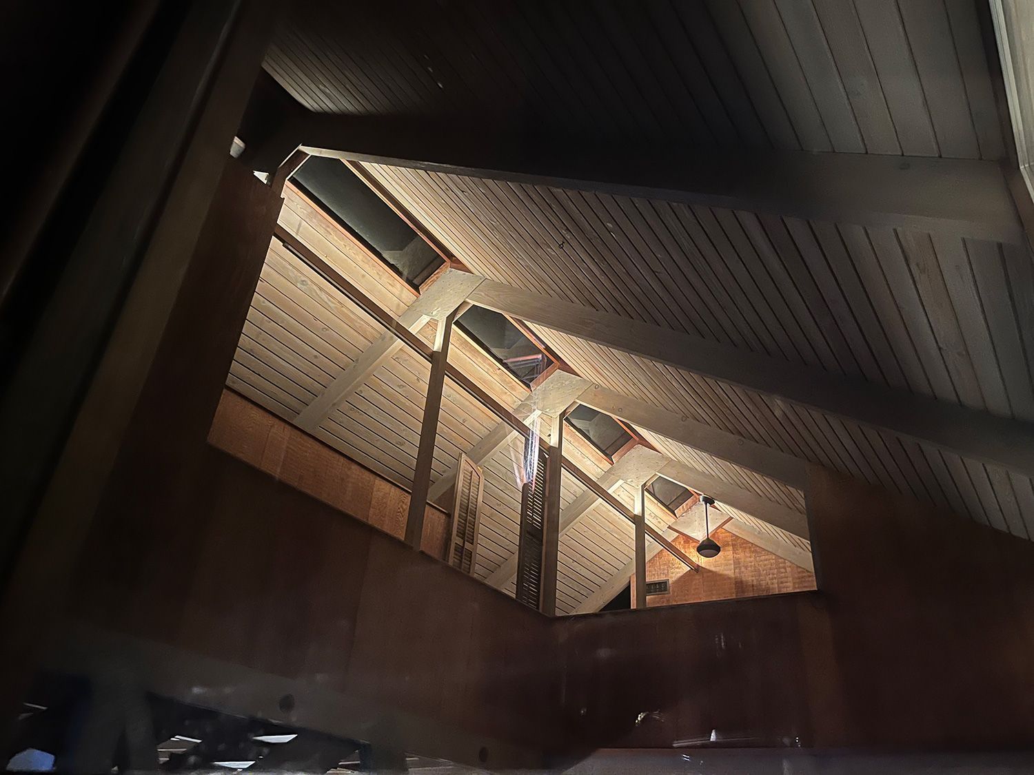 Interior view of an attic space with sunlight shining through a partially open gable window.