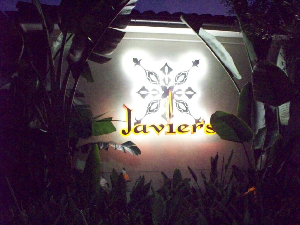 Javier's restaurant sign, illuminated at night, with ornate design and surrounded by plants.