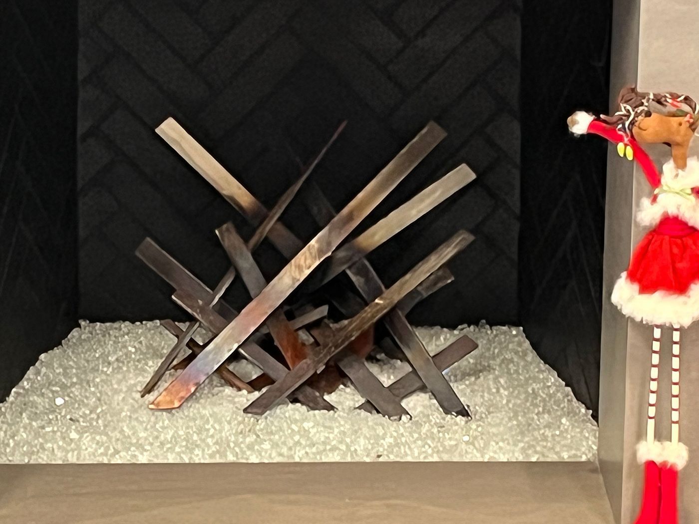 Decorative fireplace with black herringbone brick and glass beads. A festive doll stands to the right.