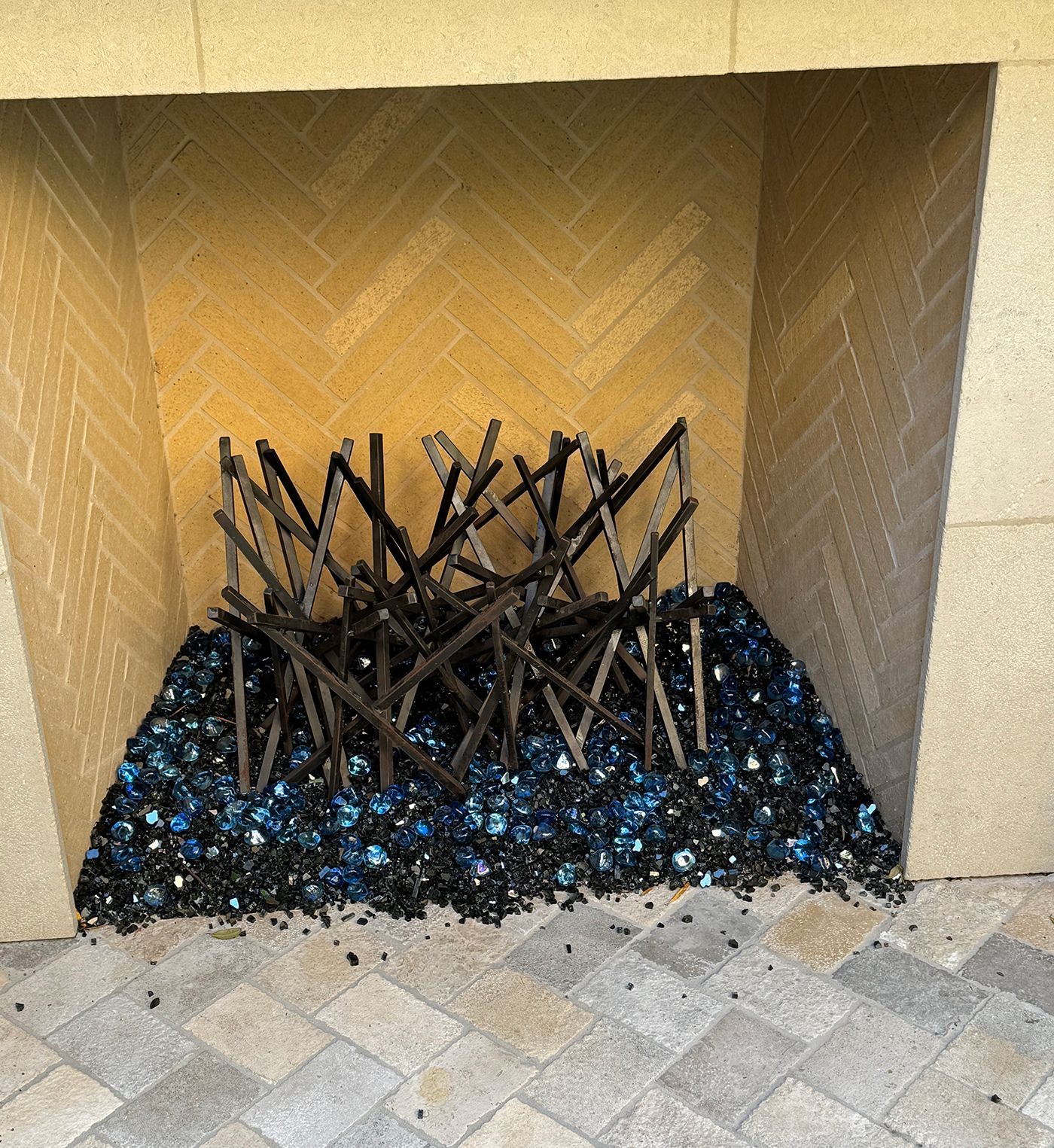 Fireplace with blue glass and metal grate against a herringbone brick background.