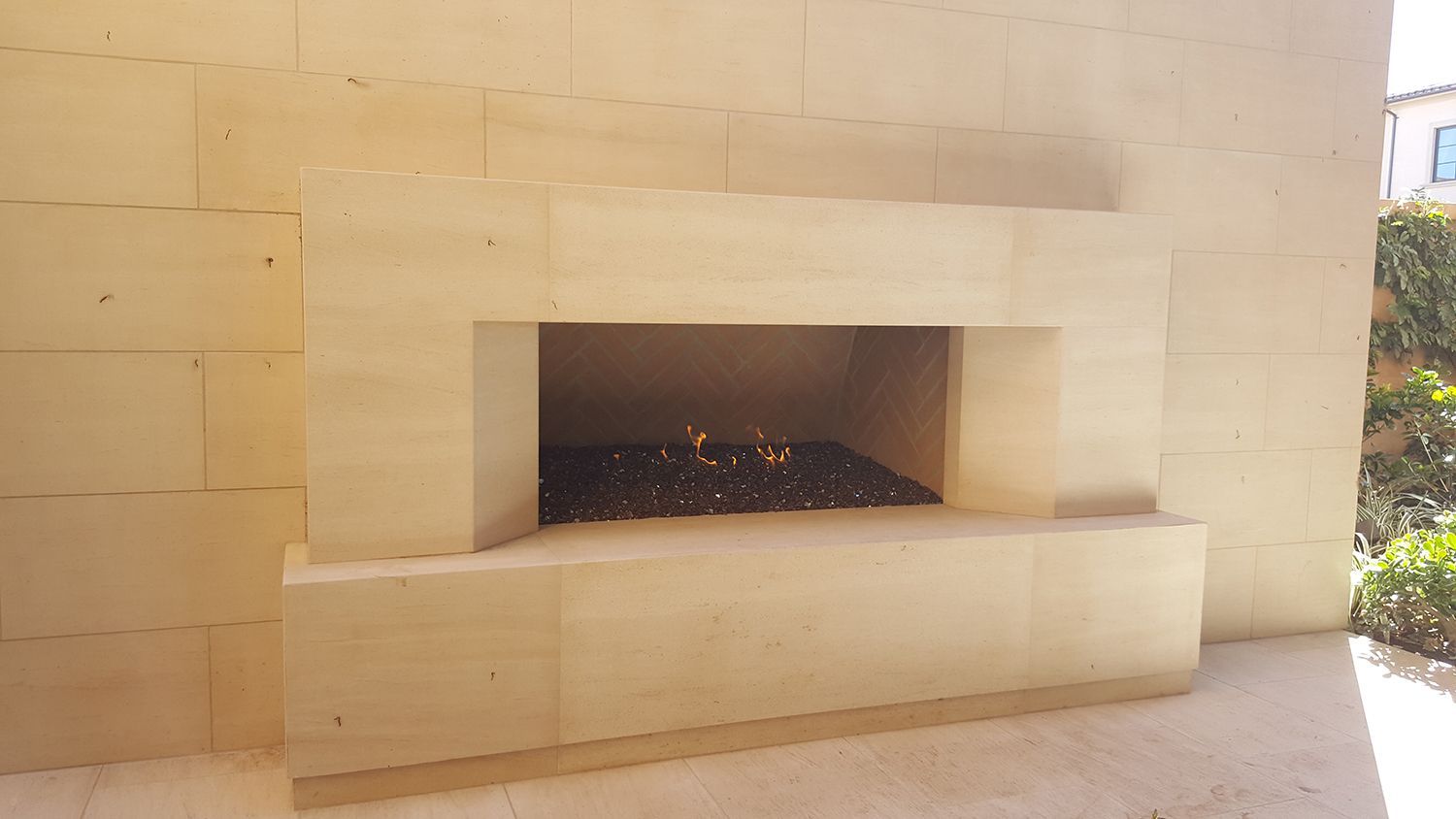 A modern outdoor fireplace with glowing embers, set in light-colored stone.