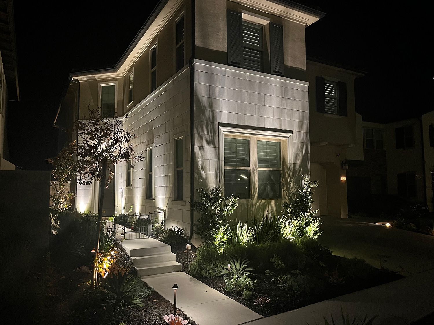 A two-story house lit up at night with landscaping and pathway lighting.