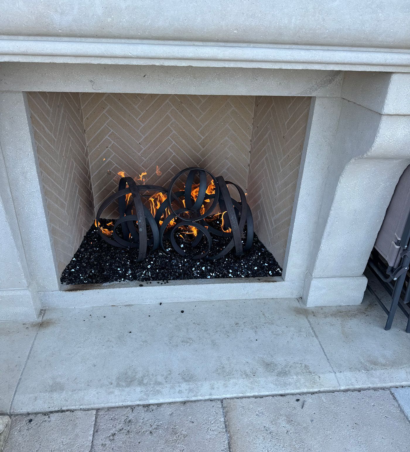 A fireplace with a metal sculpture burning on a bed of black glass stones.