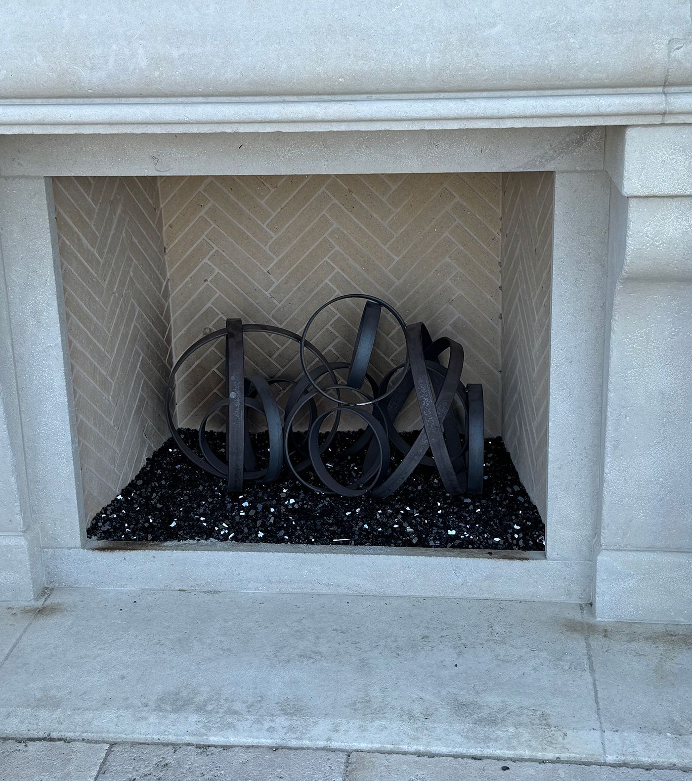 Fireplace with decorative metal sculpture and black glass fire pit rocks.