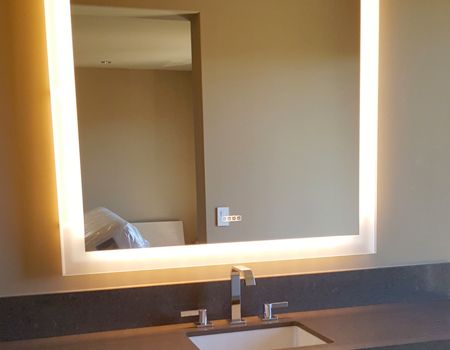 Lighted square mirror above a sink in a bathroom, neutral-colored walls, and a countertop.