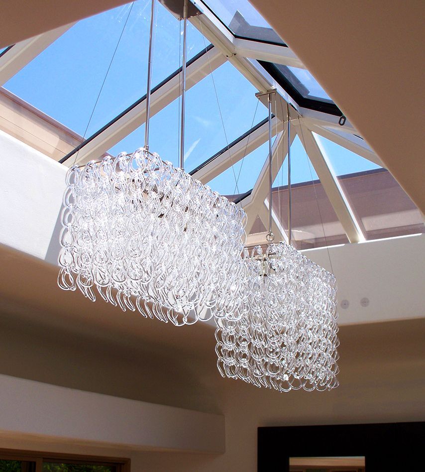 Two clear crystal chandeliers hanging from a glass ceiling with a blue sky visible.