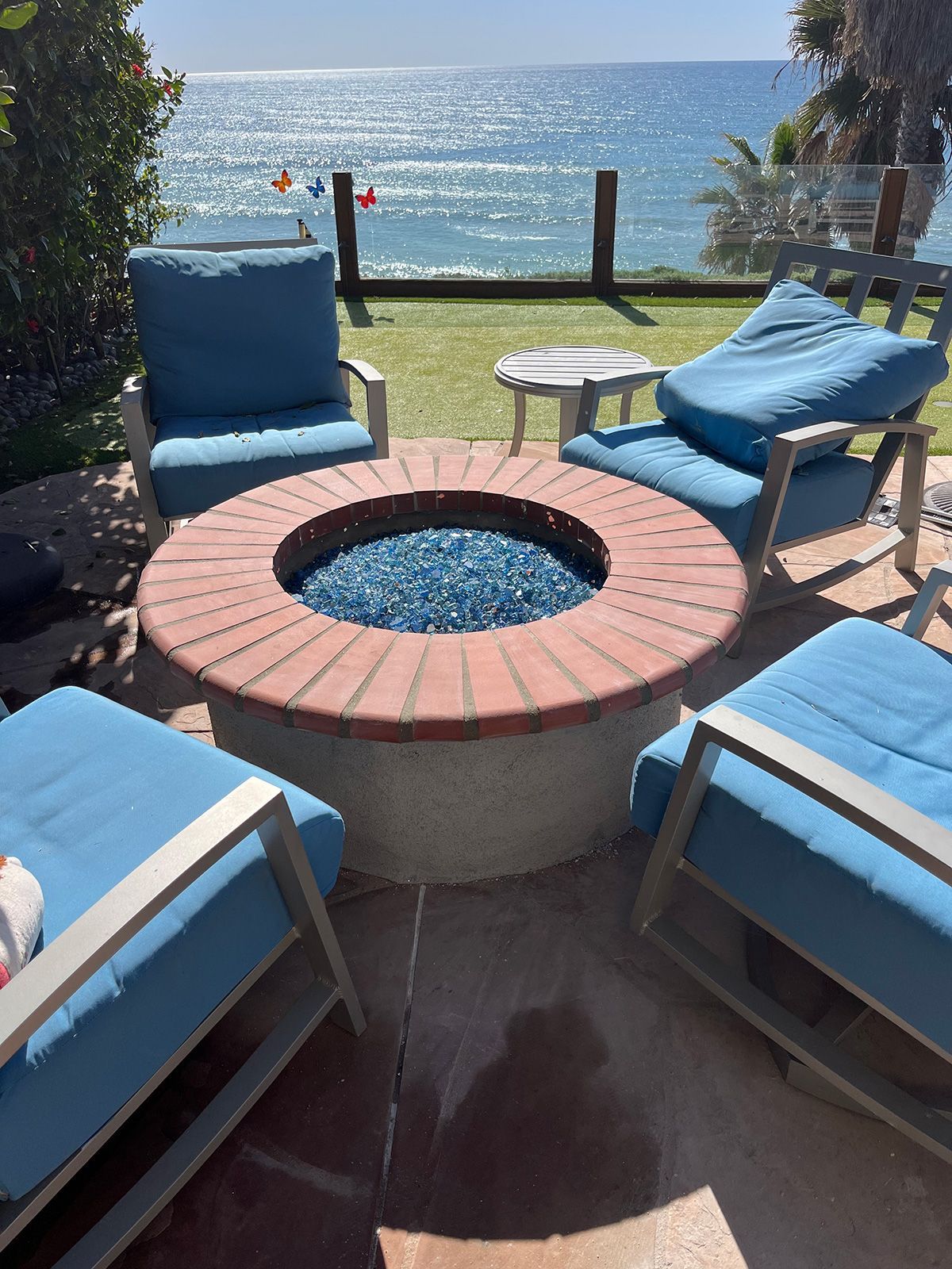 Outdoor patio with a fire pit and blue chairs overlooking the ocean.