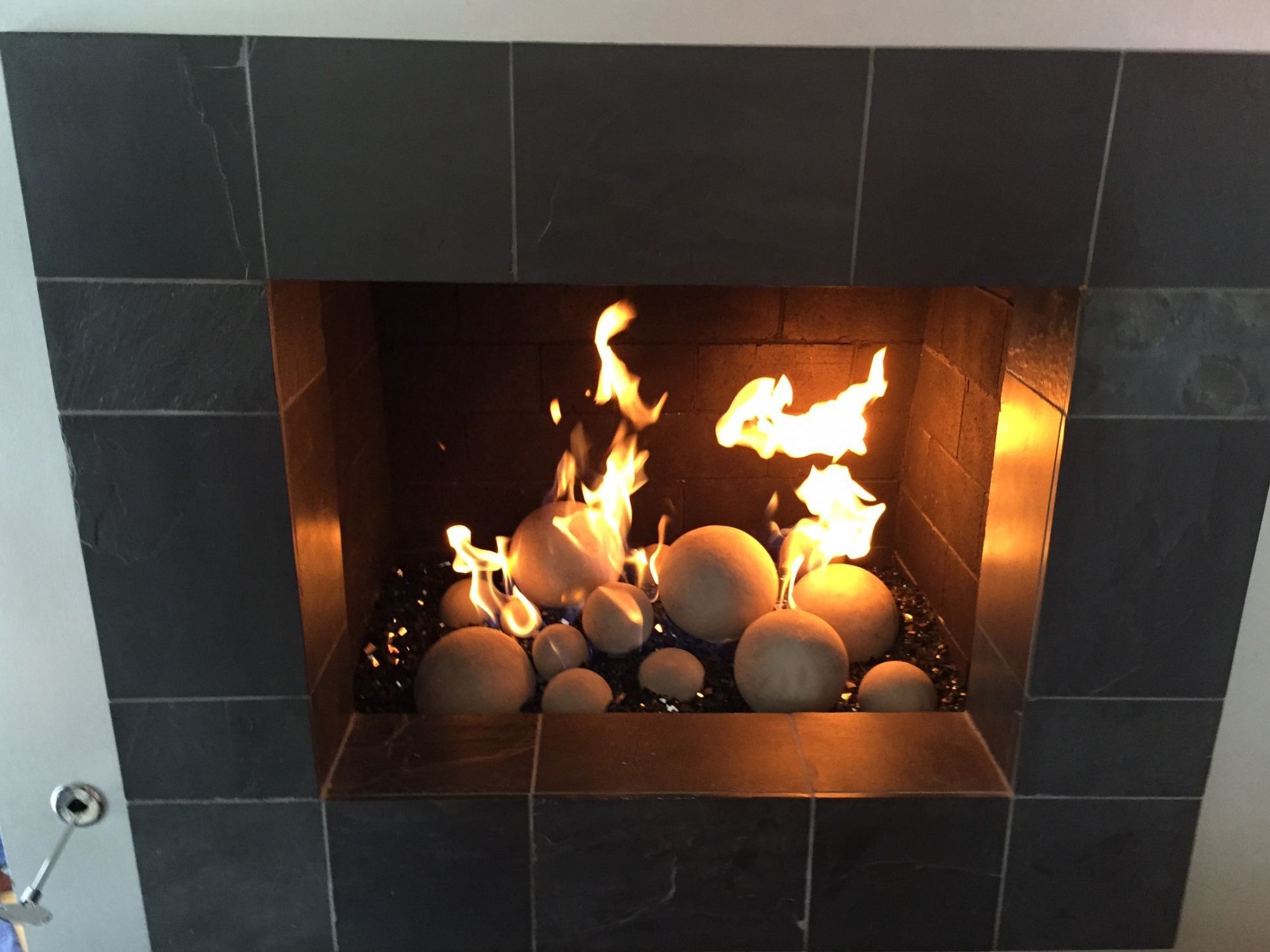 Fireplace with flames, stone balls, and dark gray tile surround.