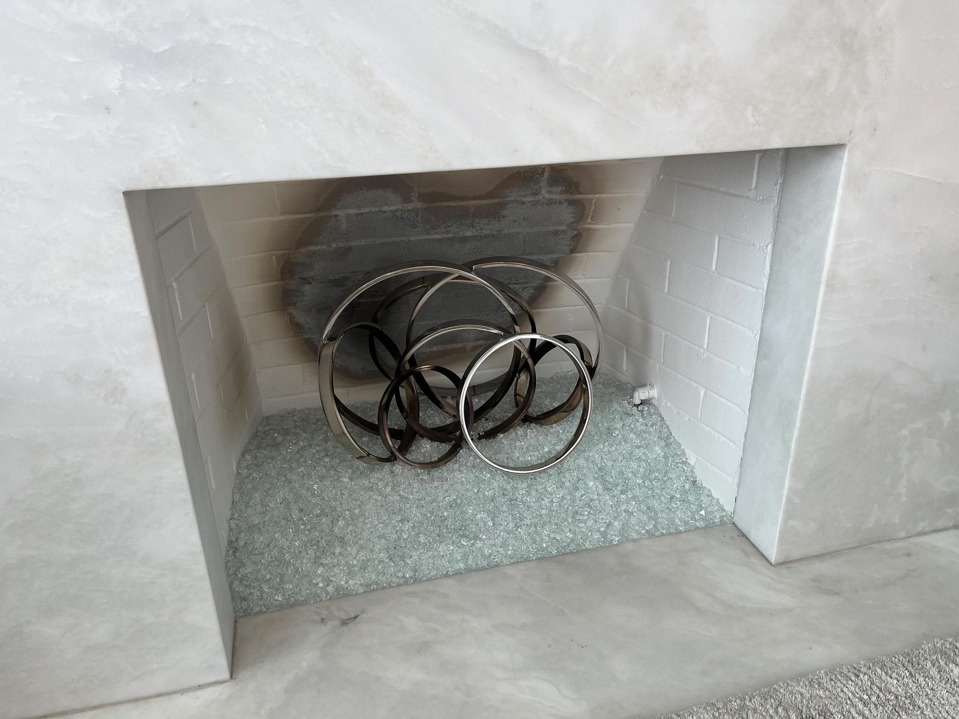 Fireplace with a metal art sculpture, blue glass, and soot stains.