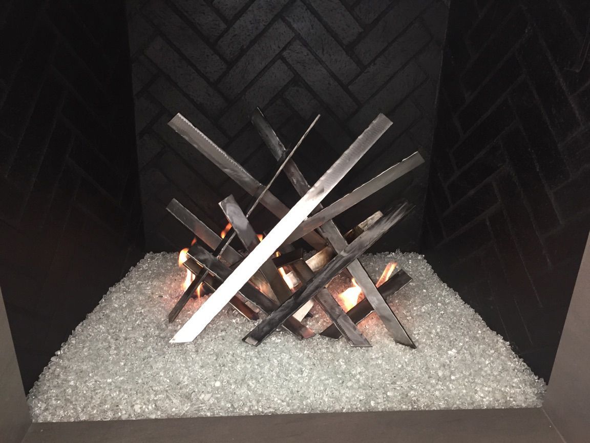 Fireplace with crisscrossed metal logs, glowing flames, and white glass stones, dark herringbone brick background.