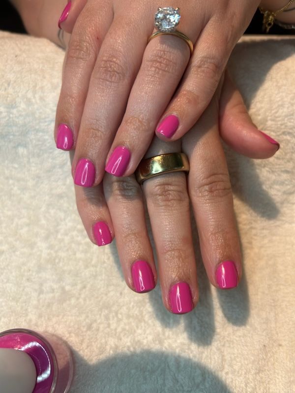 Hand with square-shaped nails painted dark purple, gold ring on middle finger, resting on a white, textured surface.