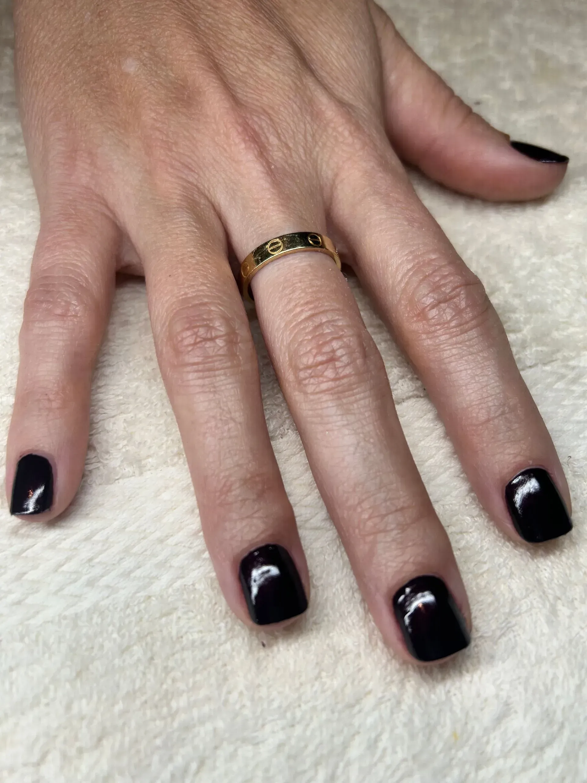 Hand with dark purple nail polish, gold ring.