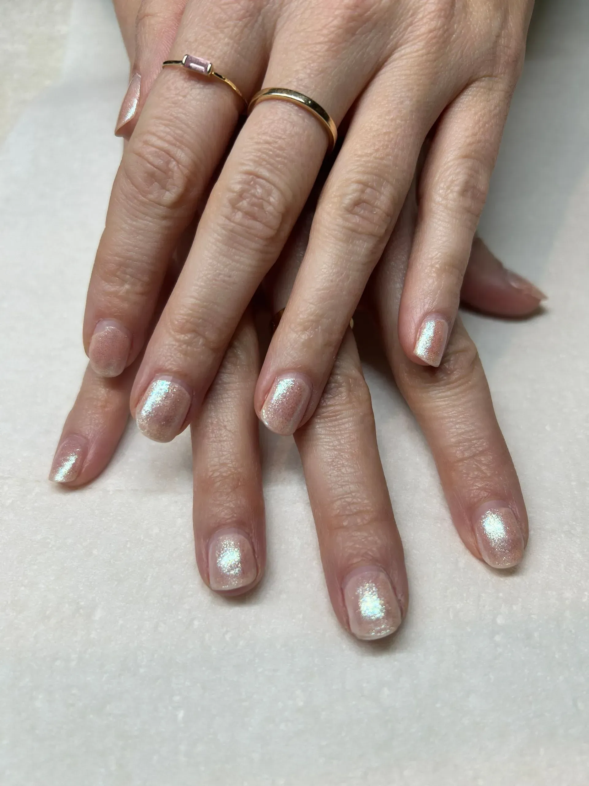 Hands with light pink iridescent nail polish, and gold rings.