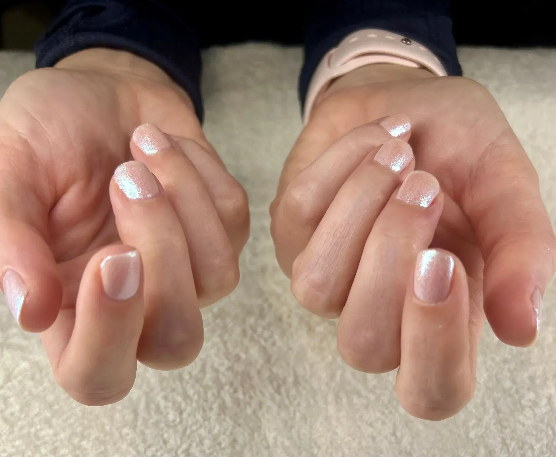 Two hands with short, light pink nails, glistening.