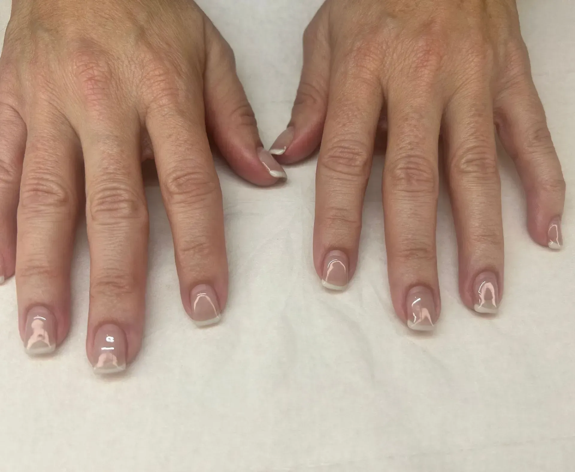 Hands with manicured nails, French tips, resting on a white surface.