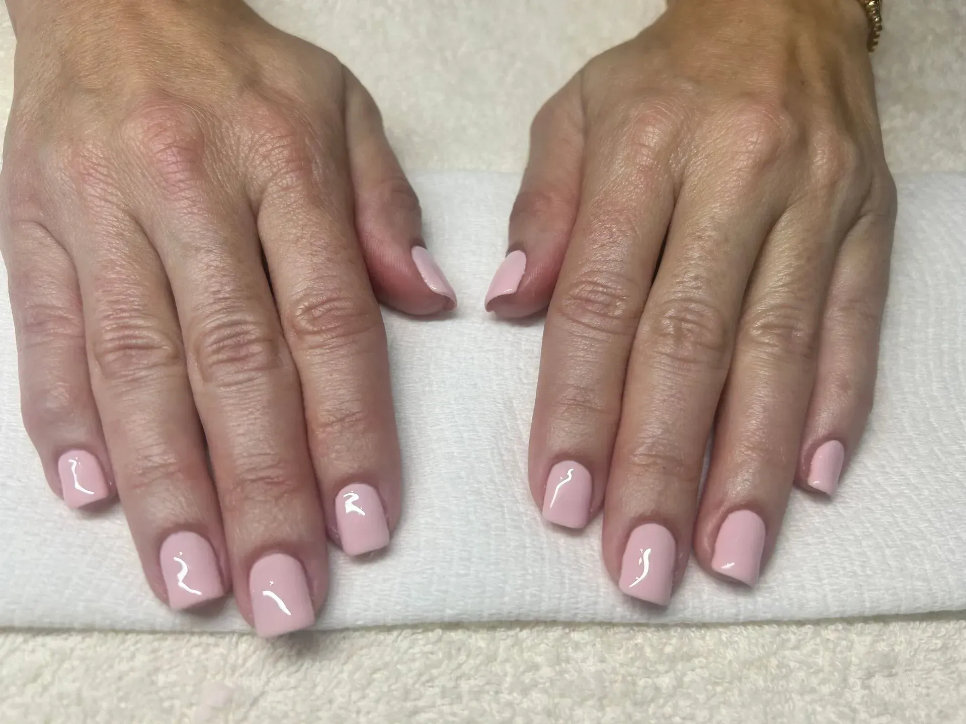 Two hands with short, light pink, manicured nails on a white towel.